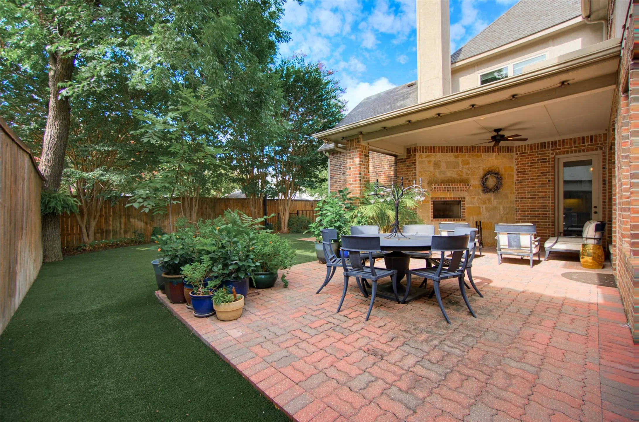 Covered outdoor living area featuring a brick and stone-clad fireplace and ceiling fan