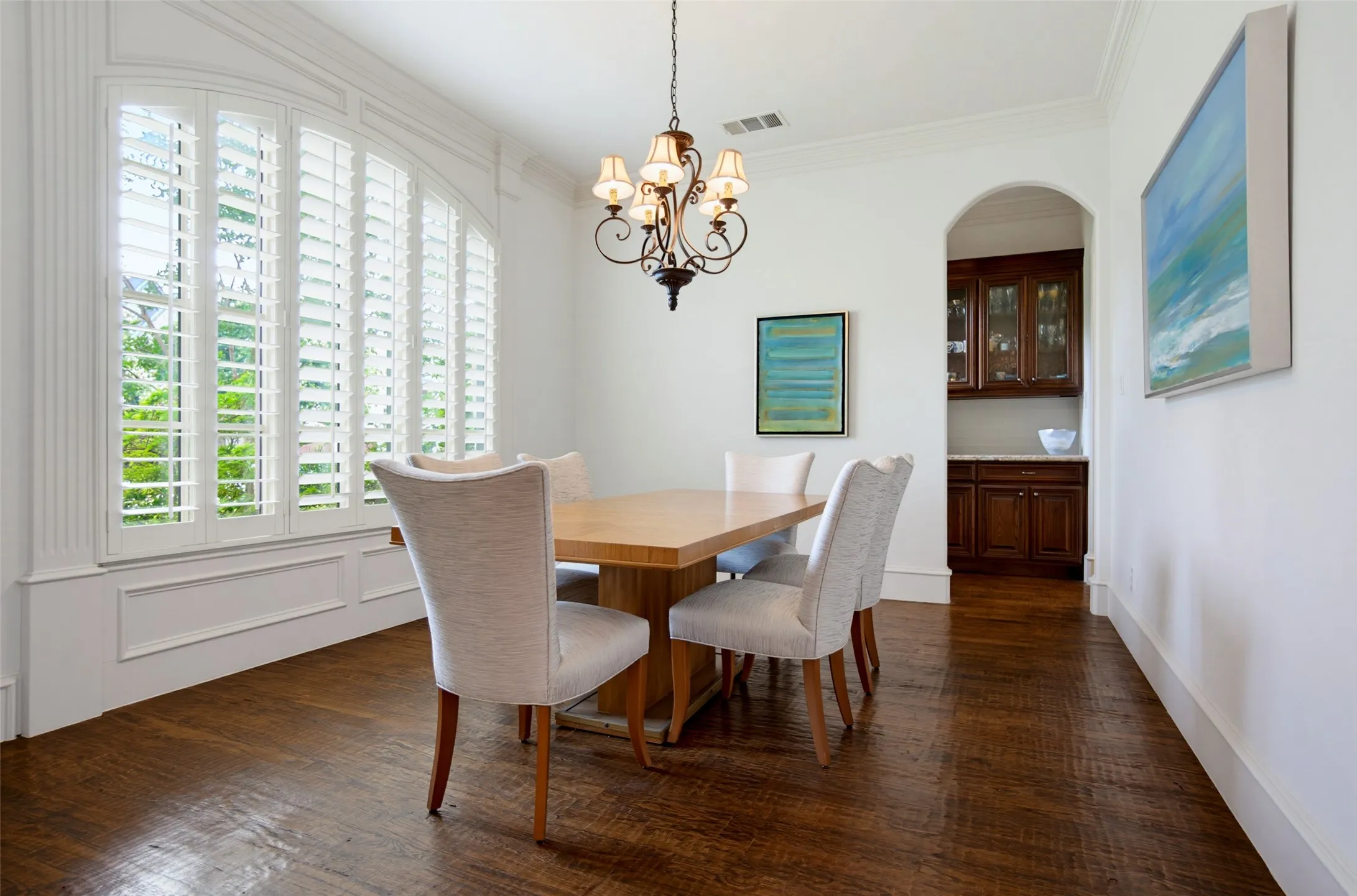 Dining area featuring an arched window with plantation shutters, wood-finish flooring, and a built-in wet bar with dark wood cabinetry