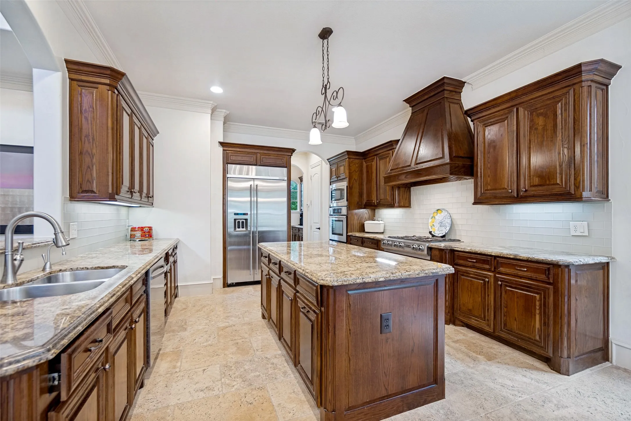 Kitchen featuring rich wood cabinetry, stone countertops, a large center island, stainless steel appliances, and a white subway tile backsplash