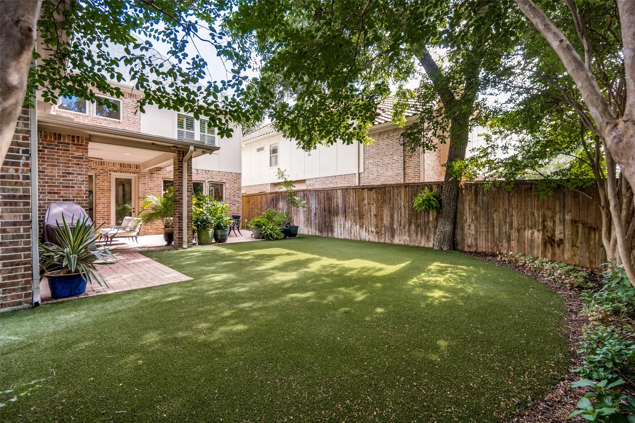 Expansive outdoor area featuring artificial turf, a brick paver patio, and a covered patio with recessed lighting