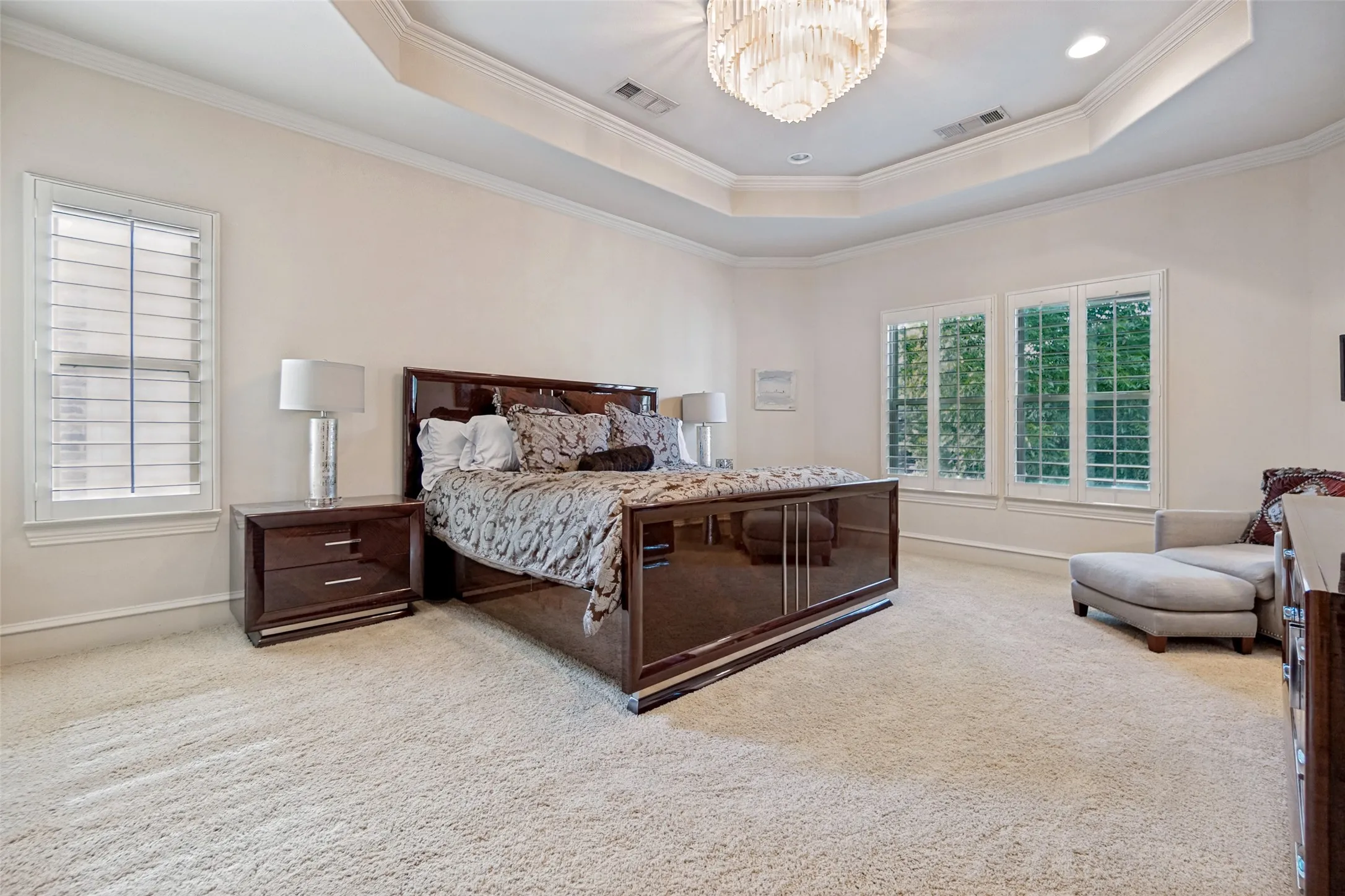 Spacious room featuring plush carpeting, elegant tray ceiling with a chandelier, multiple windows with plantation shutters, and a neutral wall palette
