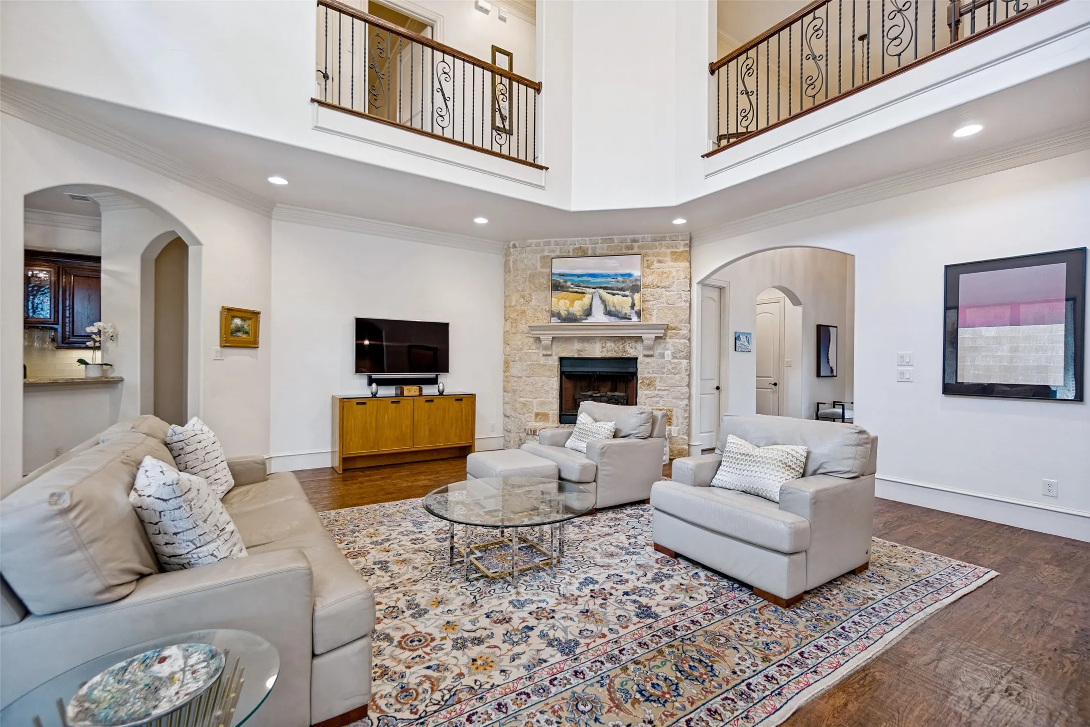Two-story living area featuring a stone-clad fireplace, dark wood-finish flooring, and arched doorways