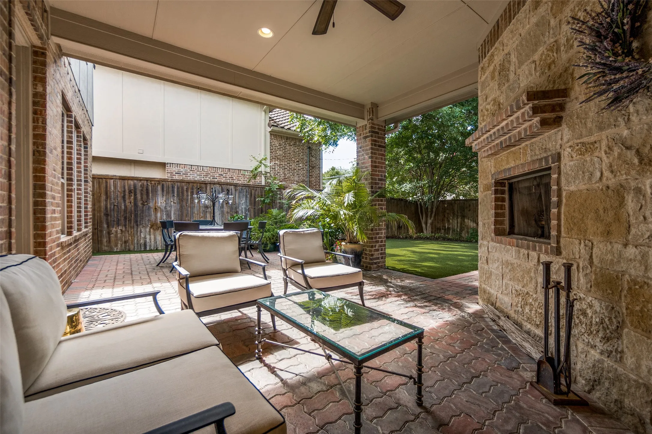 Covered patio featuring a stone-clad fireplace and brick-patterned pavers