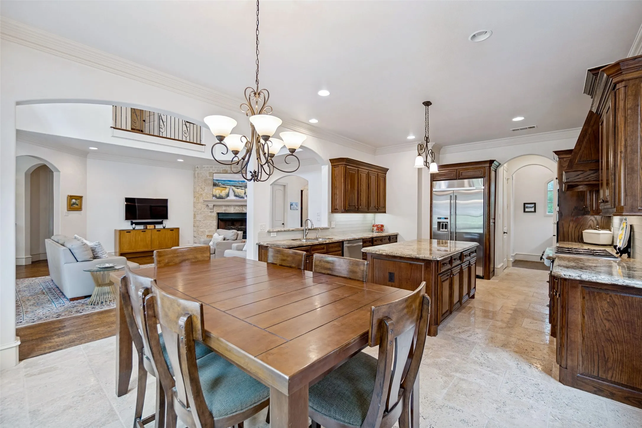 Spacious kitchen and dining area featuring stone tile flooring, dark wood cabinetry, light-toned countertops, a central island, and a chandelier