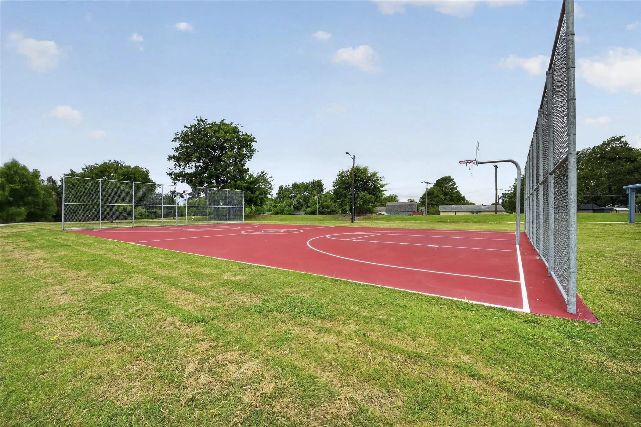 Outdoor recreational basketball court featuring a red playing surface and perimeter fencing