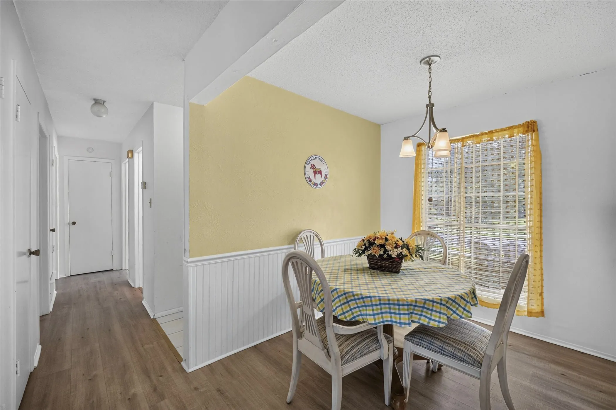 Dining area featuring a three-light chandelier, a window with horizontal muntins, and wainscoting