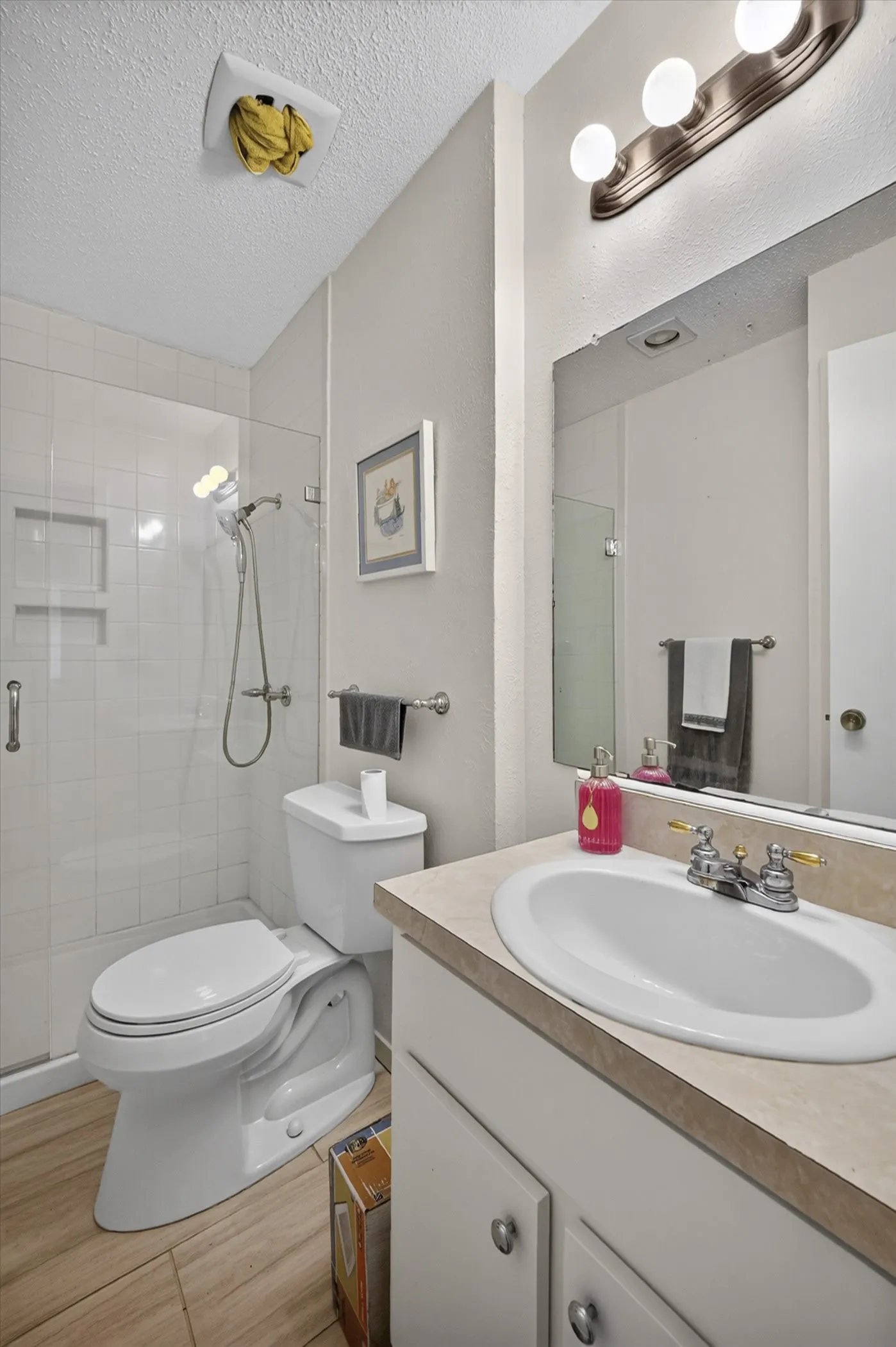 Full bathroom featuring a single vanity with an integrated sink, a glass-enclosed shower with subway tile, a toilet, and wood-finish flooring