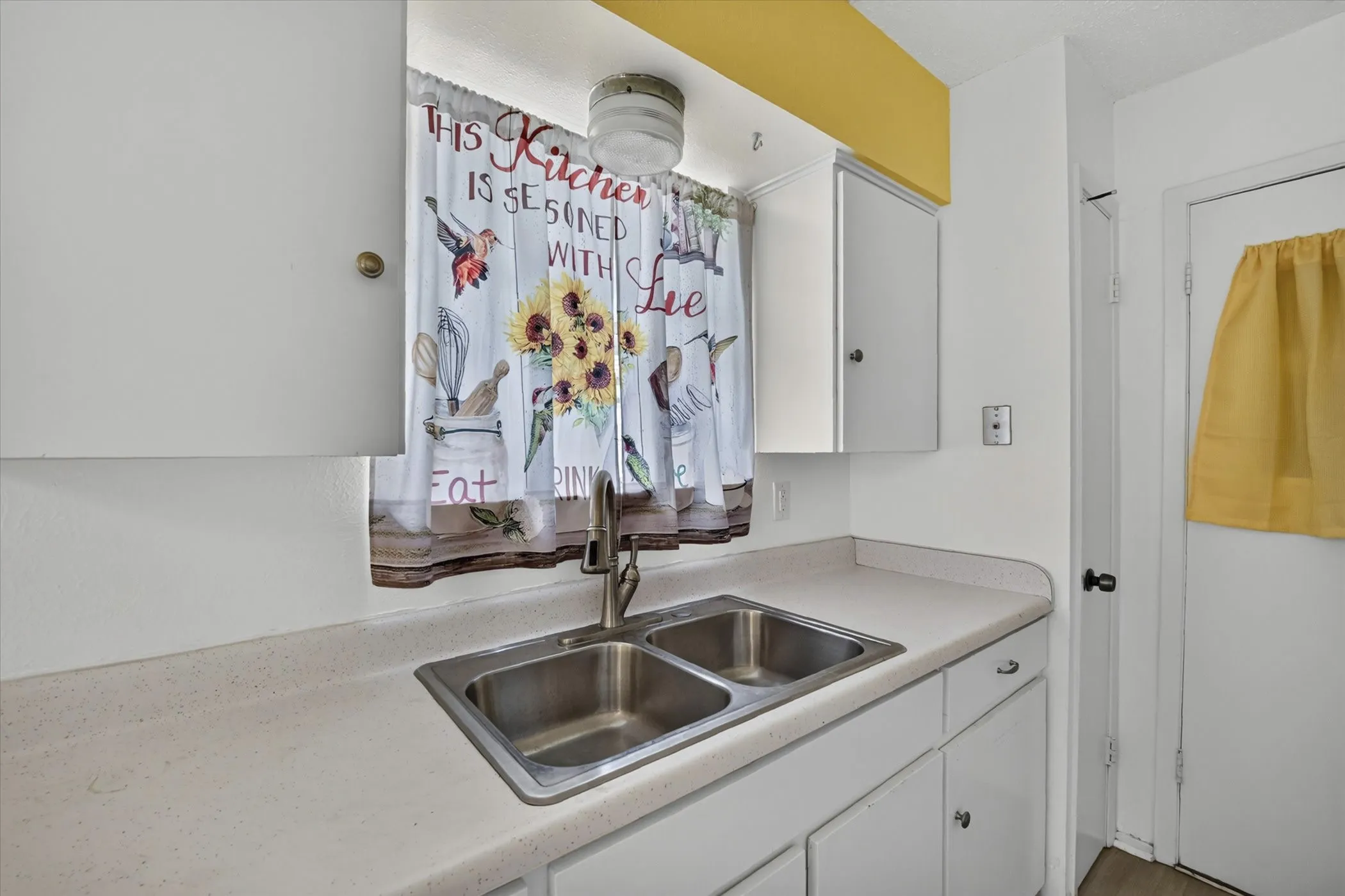 Kitchen workspace featuring a stainless steel double sink, white cabinetry, and light-toned countertops