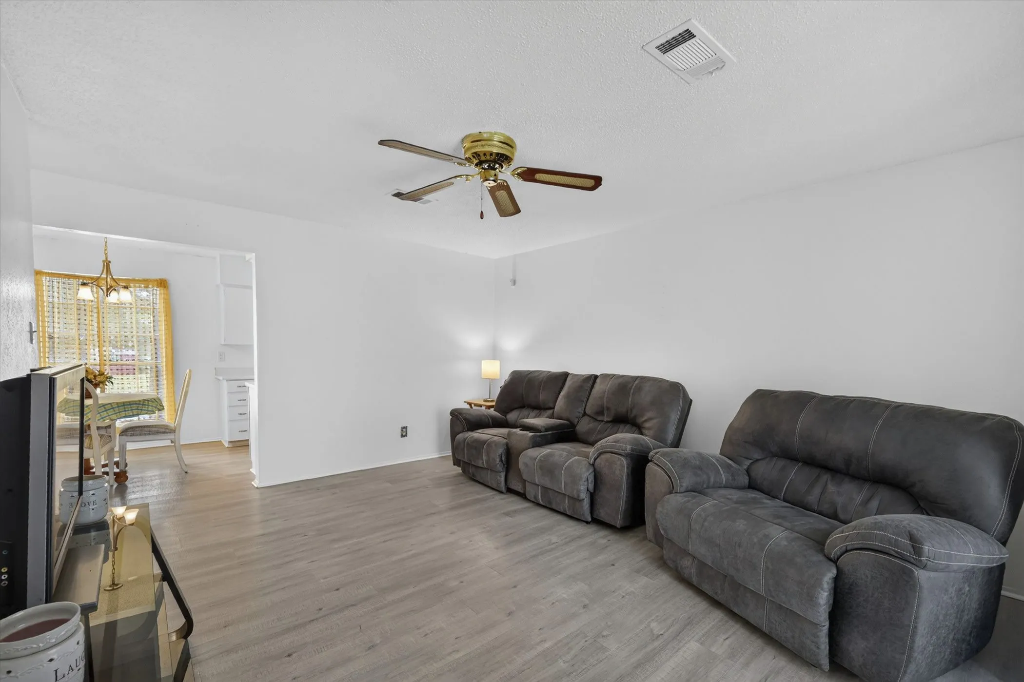 Spacious living area featuring wood-finish flooring, a ceiling fan, and white painted walls