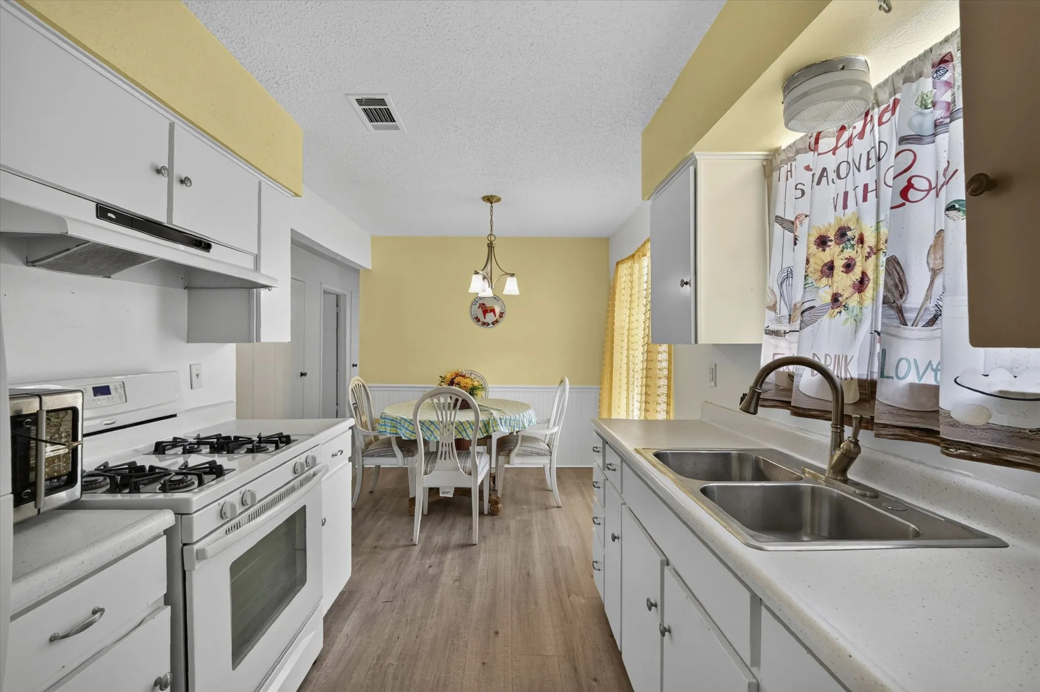 Kitchen and dining area featuring white cabinetry, light-toned flooring, and a double basin sink
