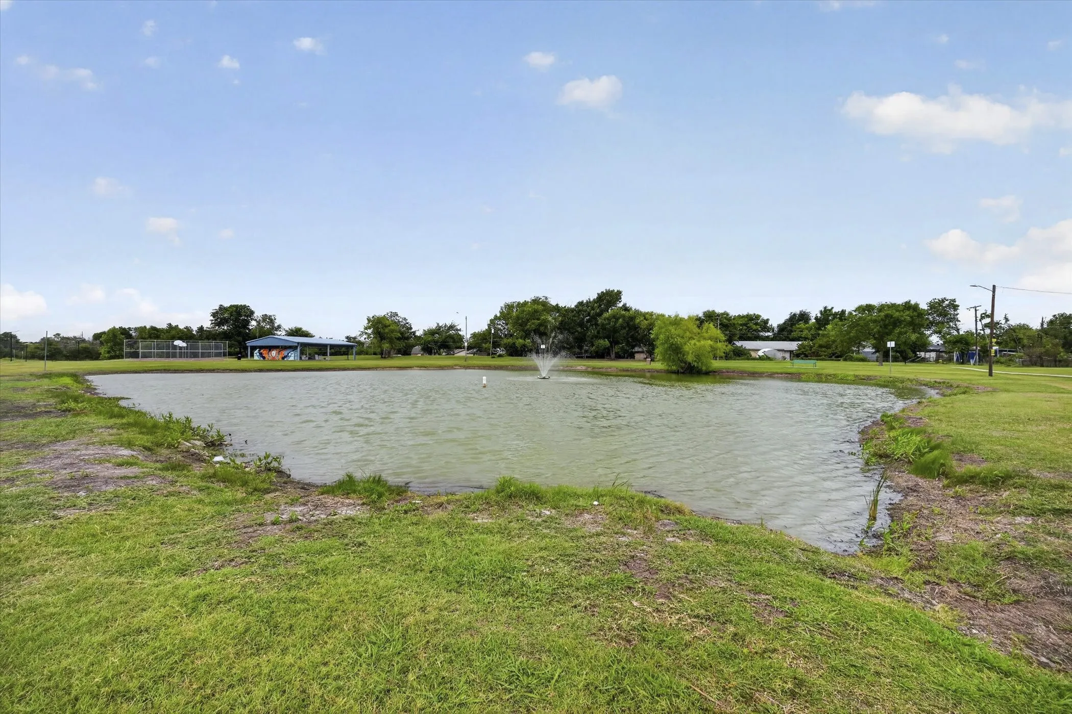 Pond with an active fountain feature surrounded by a grassy bank and distant trees