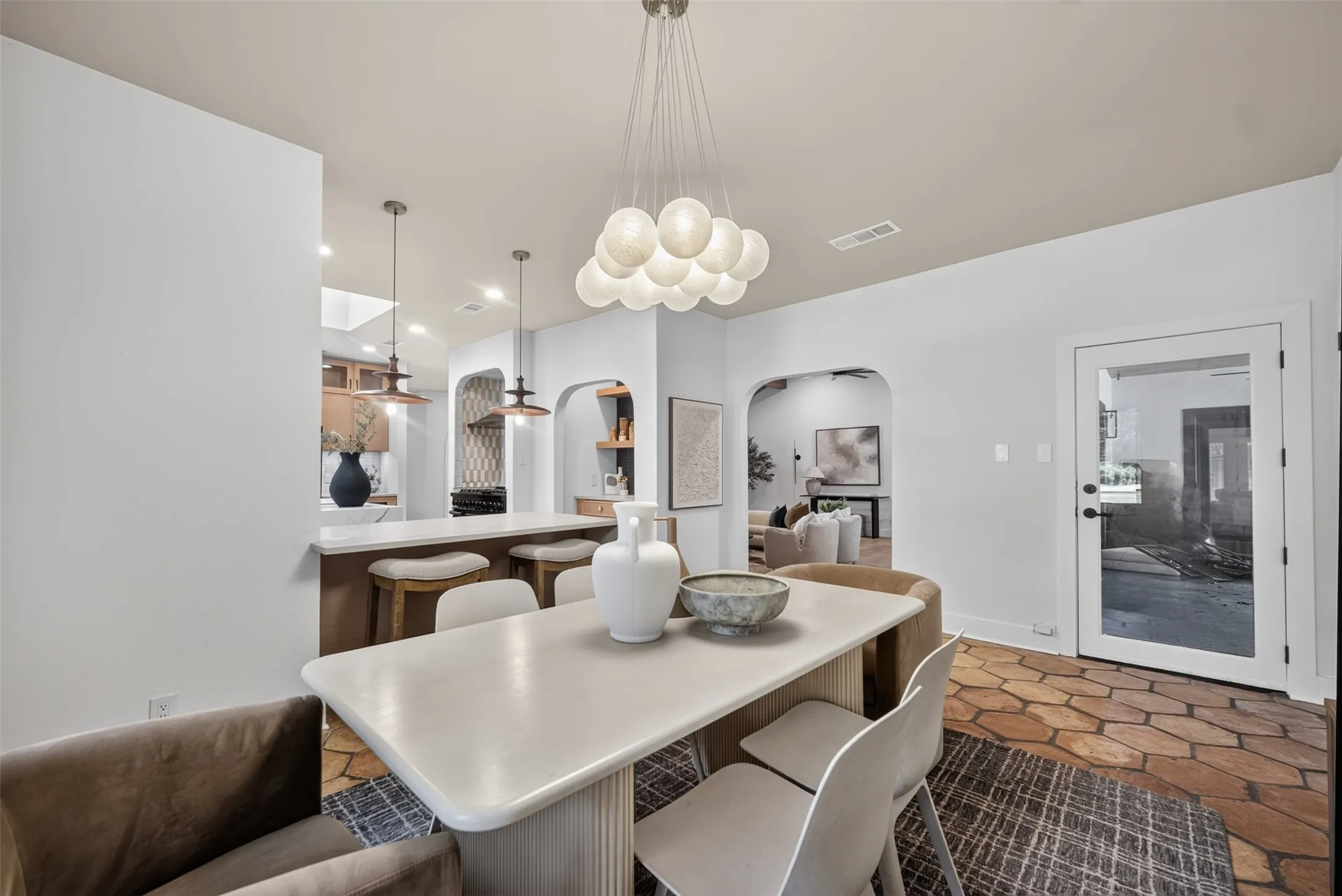 Dining area featuring a contemporary chandelier, light-toned walls, and terracotta-style hexagonal floor tiles