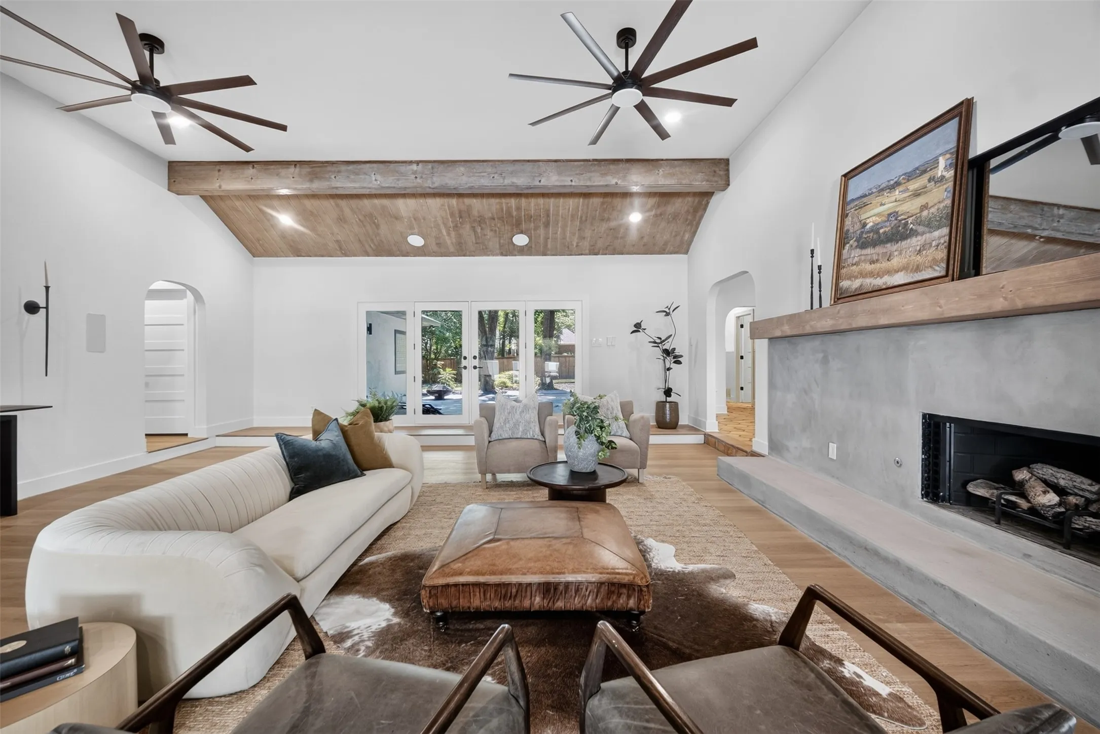 Vaulted ceilings with exposed wood beams, a modern fireplace with a wood-mantel, wood-finish flooring, recessed lighting, and a double-door exterior entry