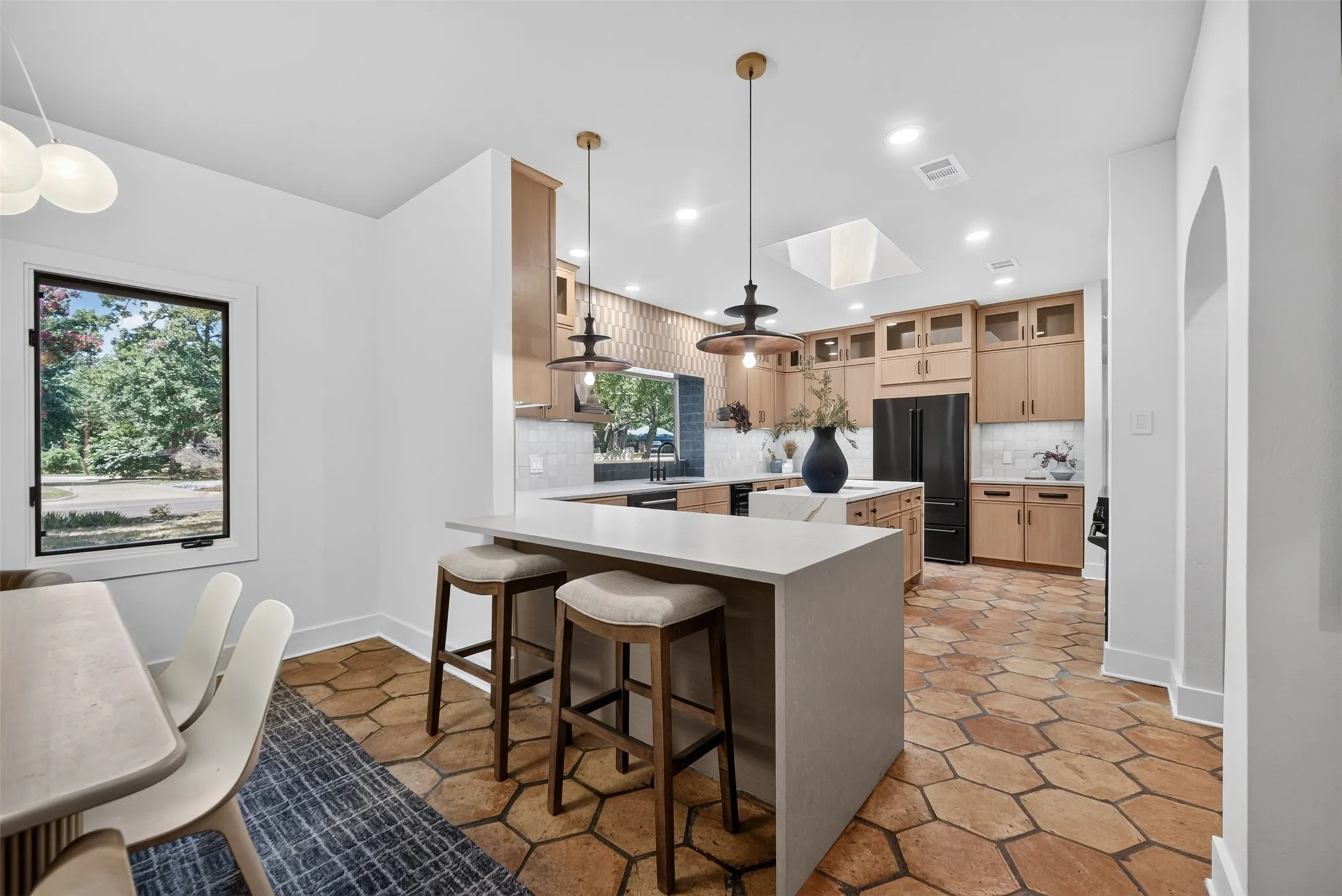 Kitchen featuring a center island with bar seating, light wood-finish cabinetry, black stainless steel appliances, a tile backsplash, and hexagonal tile flooring