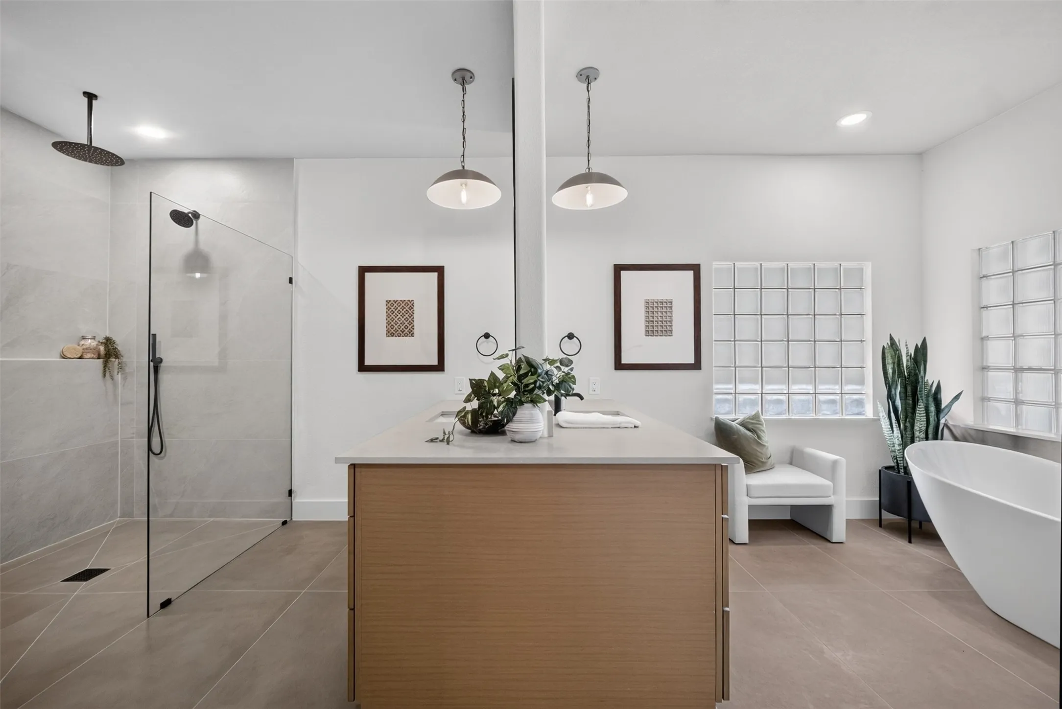 Spacious bathroom featuring a glass-enclosed shower with a rainfall showerhead and handheld sprayer, a freestanding soaking tub, a double vanity with light wood-finish cabinetry, and two glass block windows