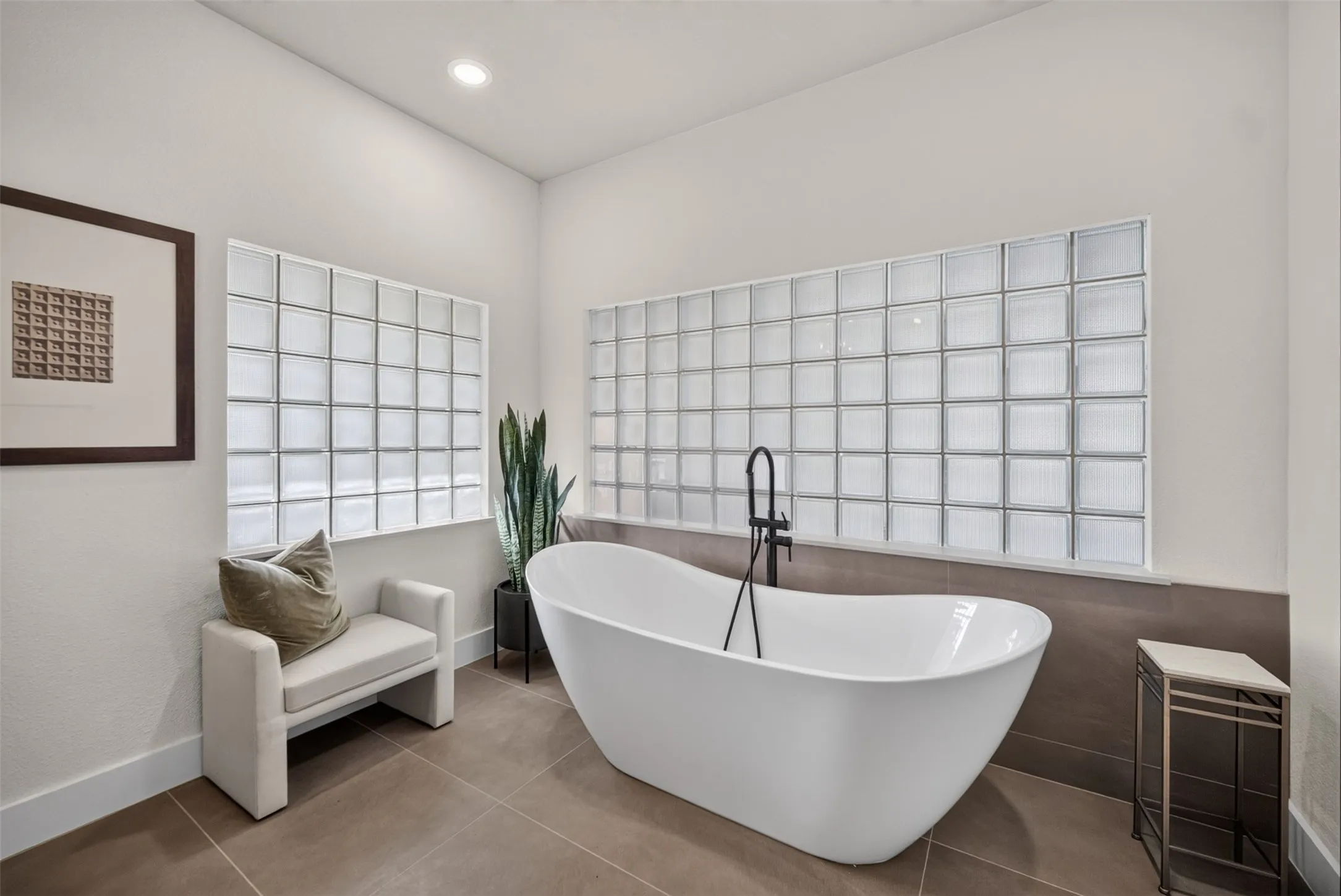 Freestanding soaking tub with a floor-mounted matte black faucet, set against a wall of glass block windows
