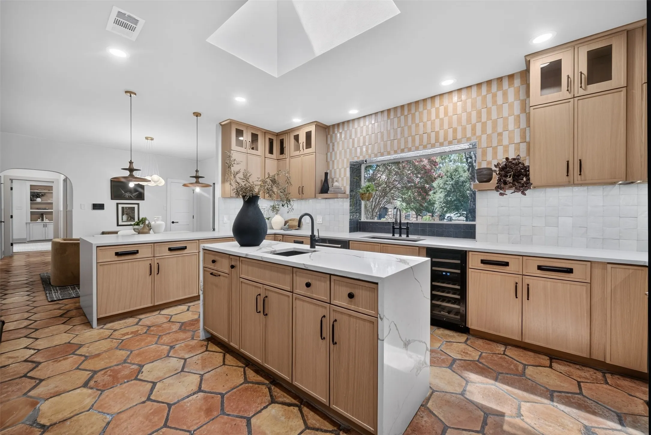 Kitchen featuring hexagon terracotta tile flooring, light wood-finish cabinetry, white countertops, and a prominent kitchen island with a built-in beverage cooler