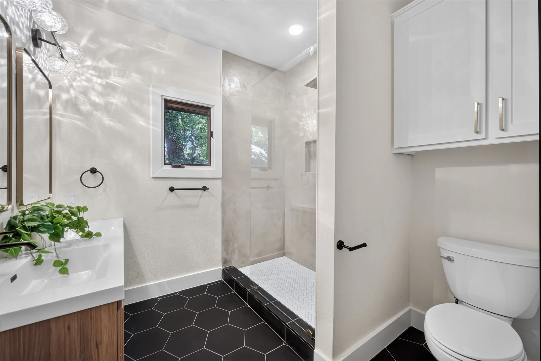 Bathroom featuring a glass-enclosed shower, black hexagonal floor tiling, and a wood-finish vanity with an integrated sink