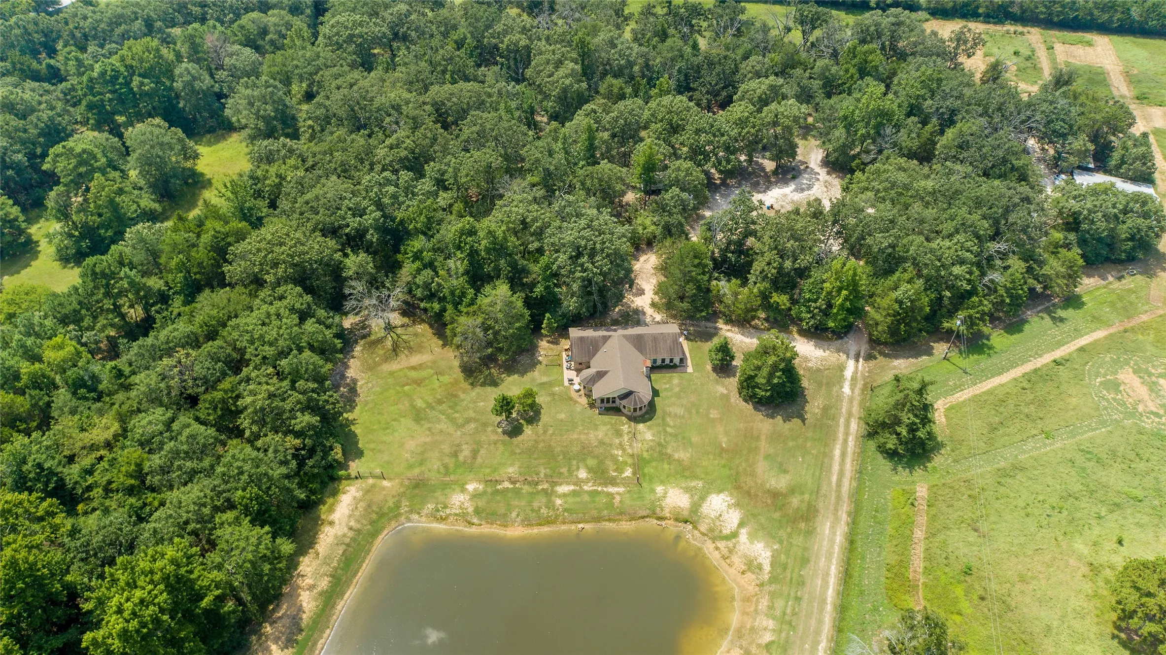 Bird eye drone view of the custom ranch home, private pond, and dense perimeter trees.