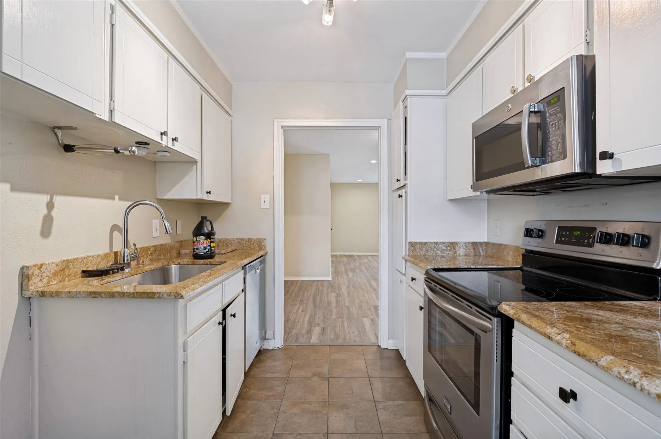 Galley kitchen featuring white cabinetry, stone-finish countertops, and stainless steel appliances including an oven range and built-in microwave