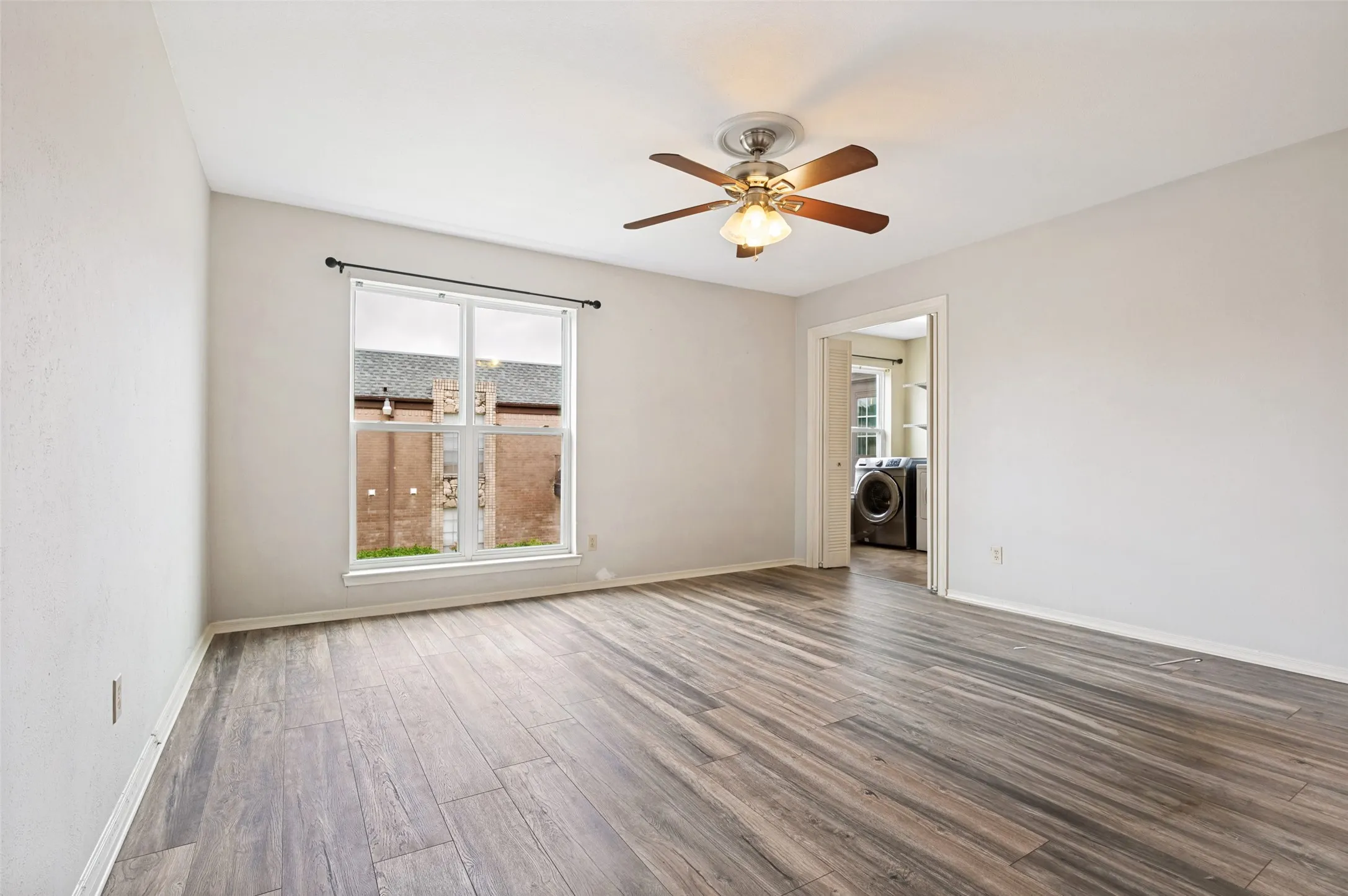 Light-filled room featuring wood-finish flooring, a ceiling fan with integrated lighting, and a white-trimmed window