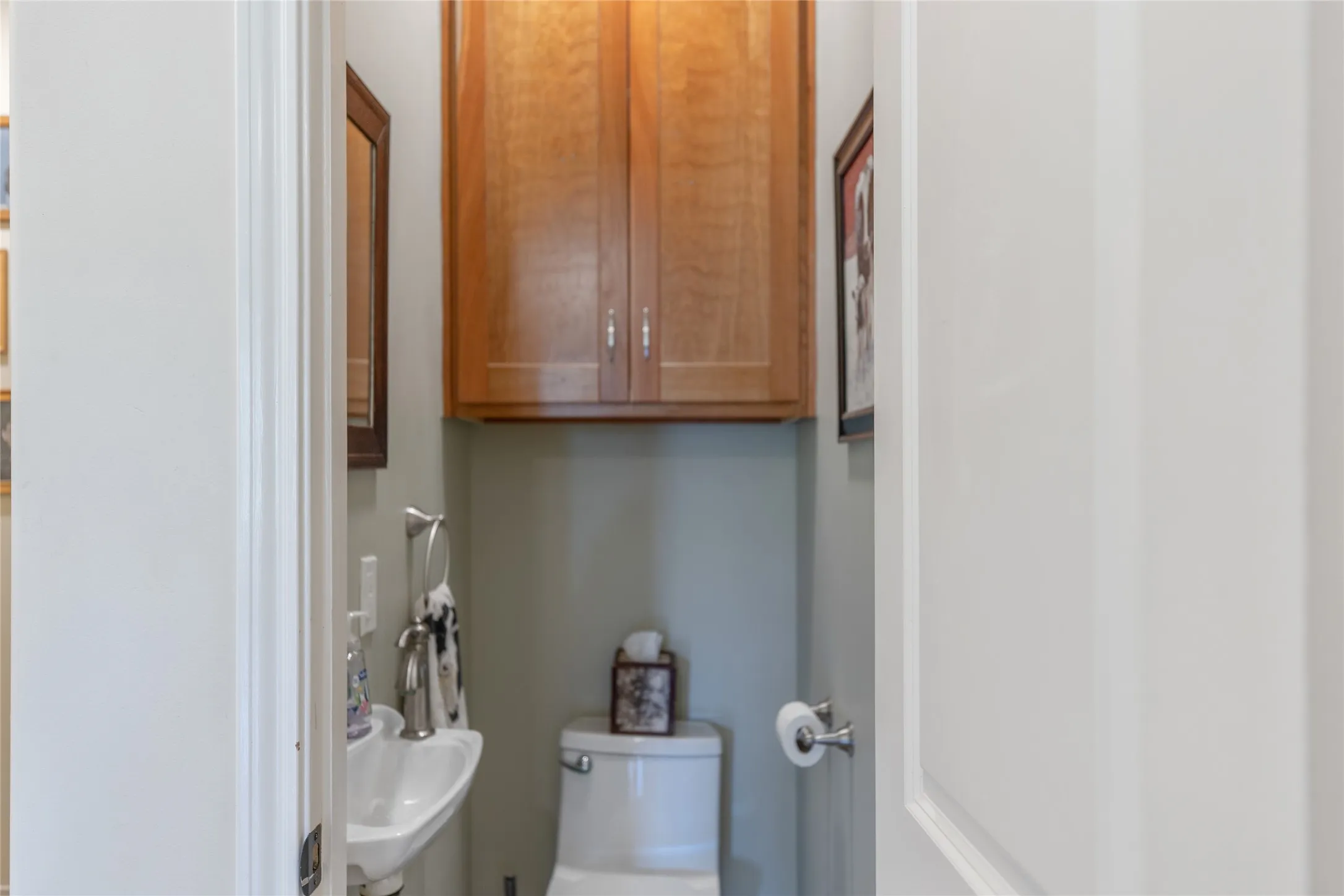 Half bath powder room featuring a toilet, sink, and custom wood storage cabinets.