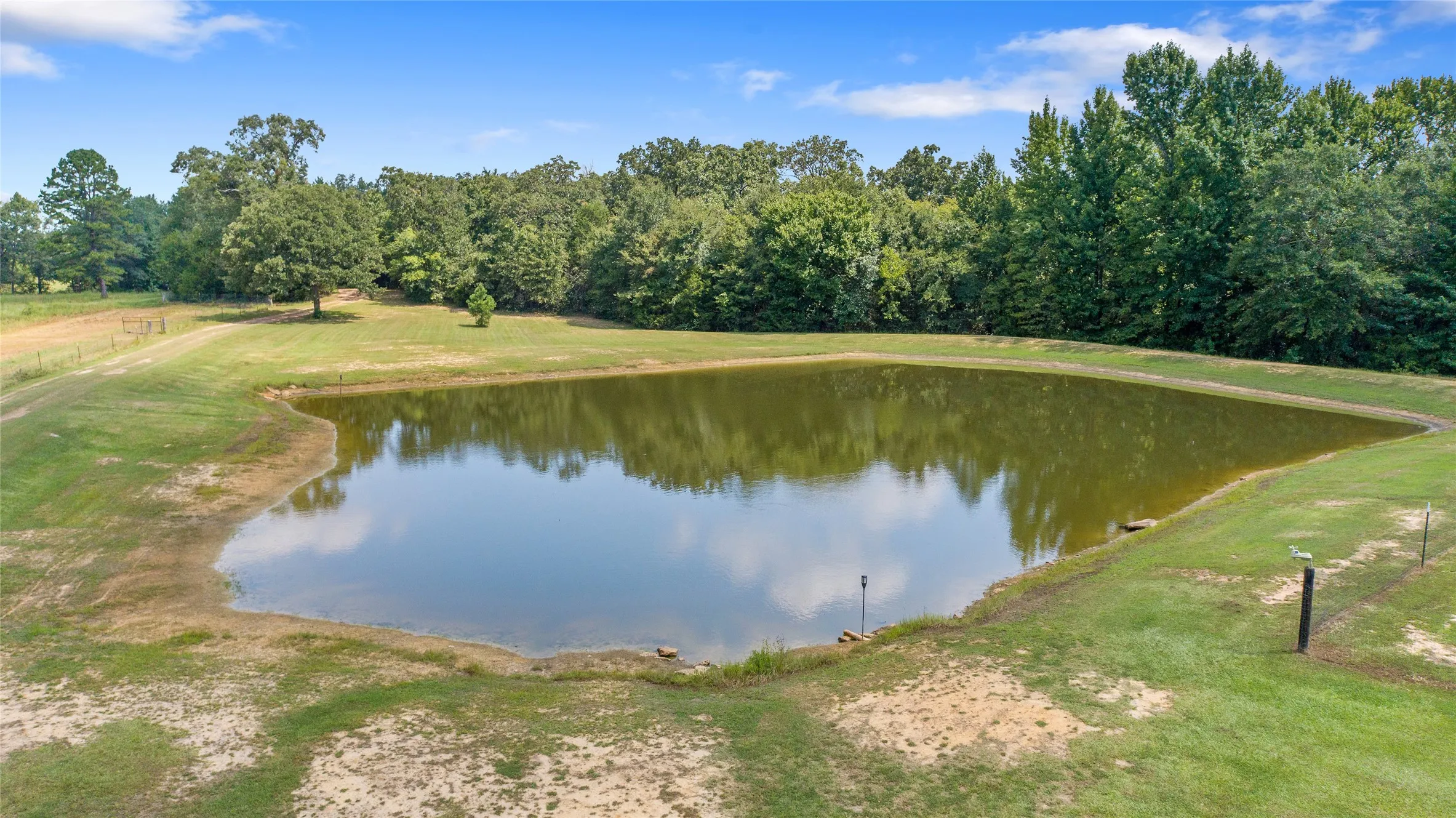 Clear water view of the private half acre stock pond surrounded by lush green grass.