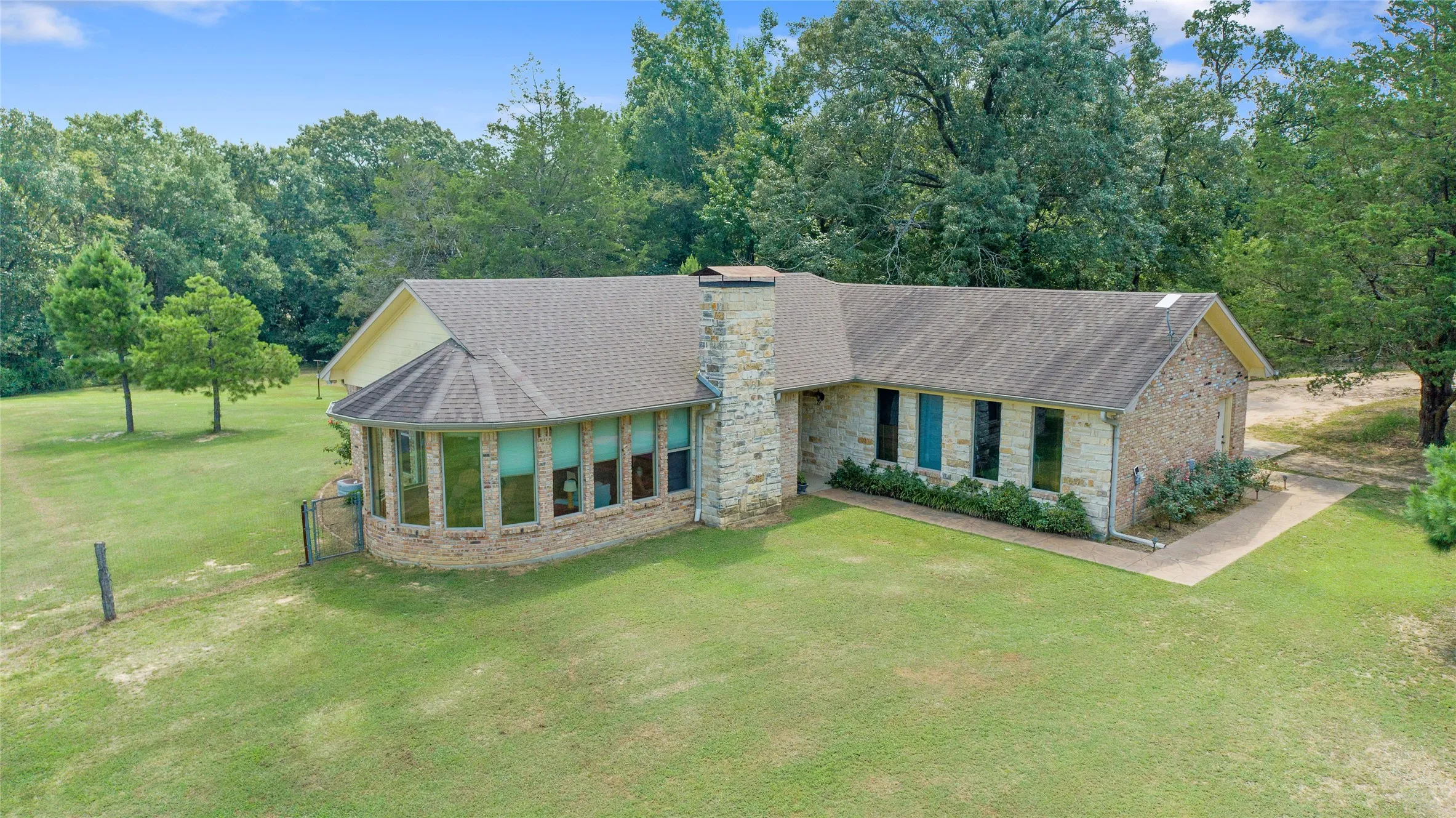 Exterior of custom brick ranch home in Wood County featuring a sunroom and mature shade trees.