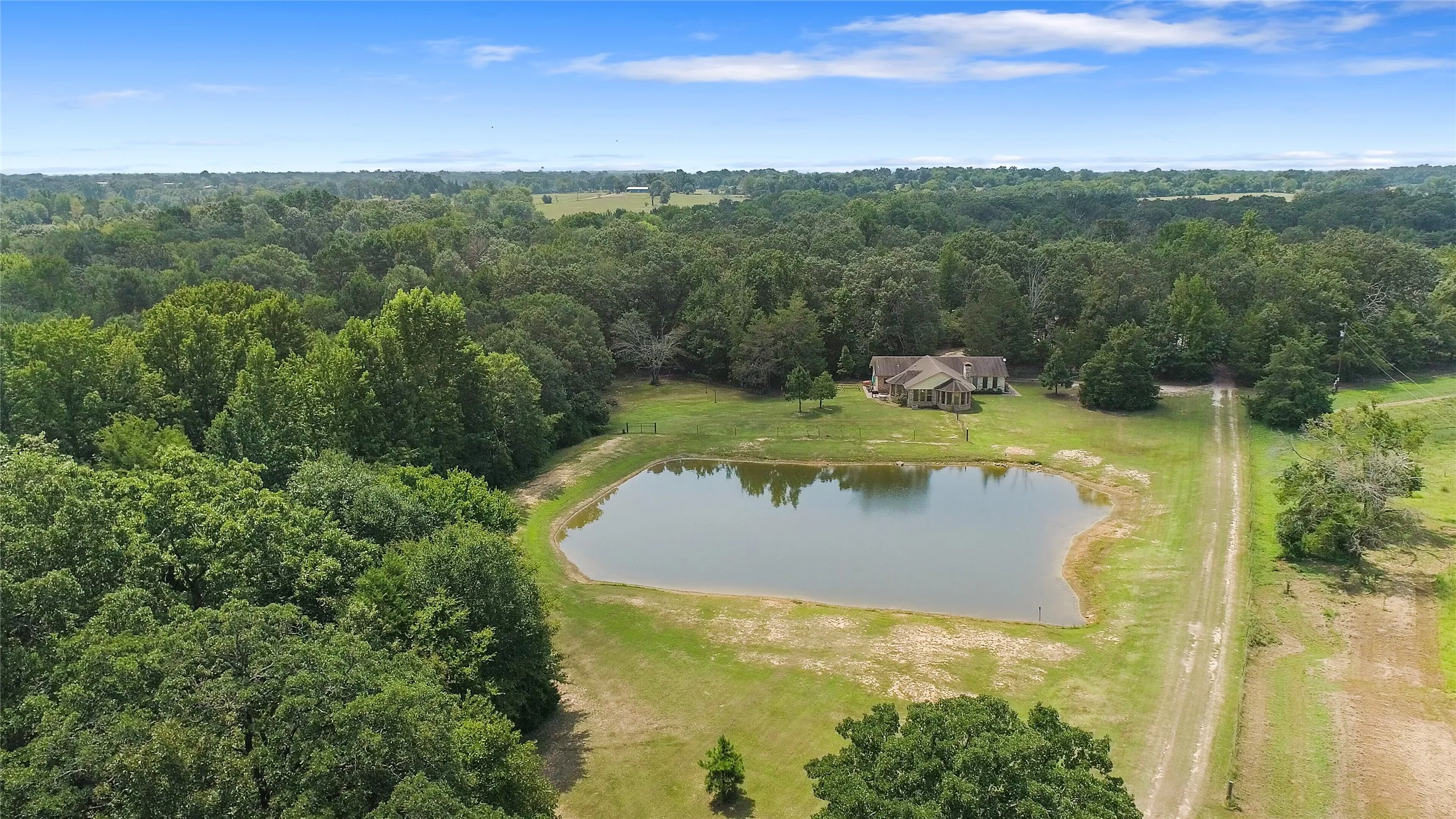 High angle drone view of the private pond, custom home, and mature trees in Wood County.
