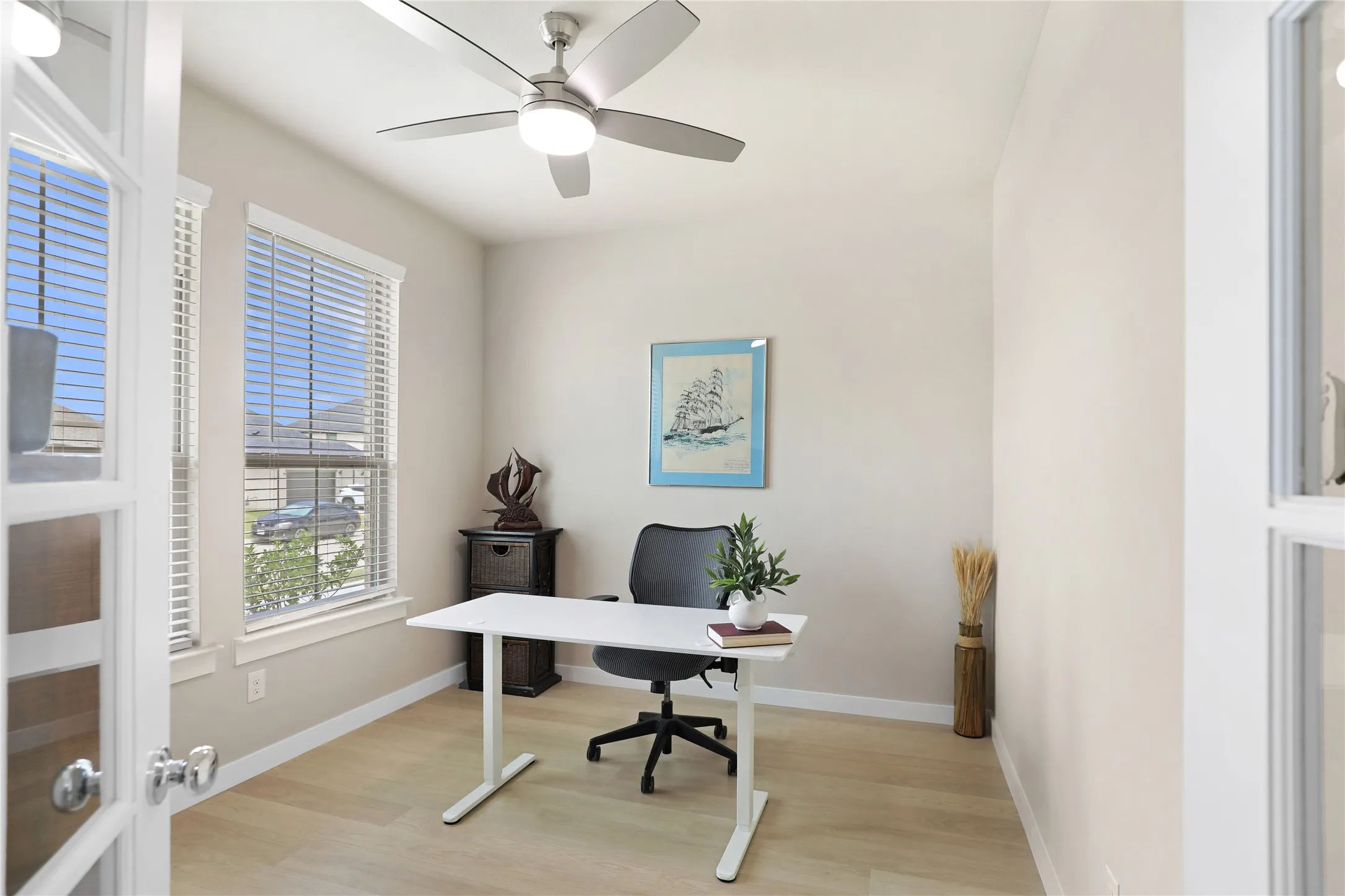 Versatile room featuring two large windows with blinds, light wood-finish flooring, and a ceiling fan with integrated lighting