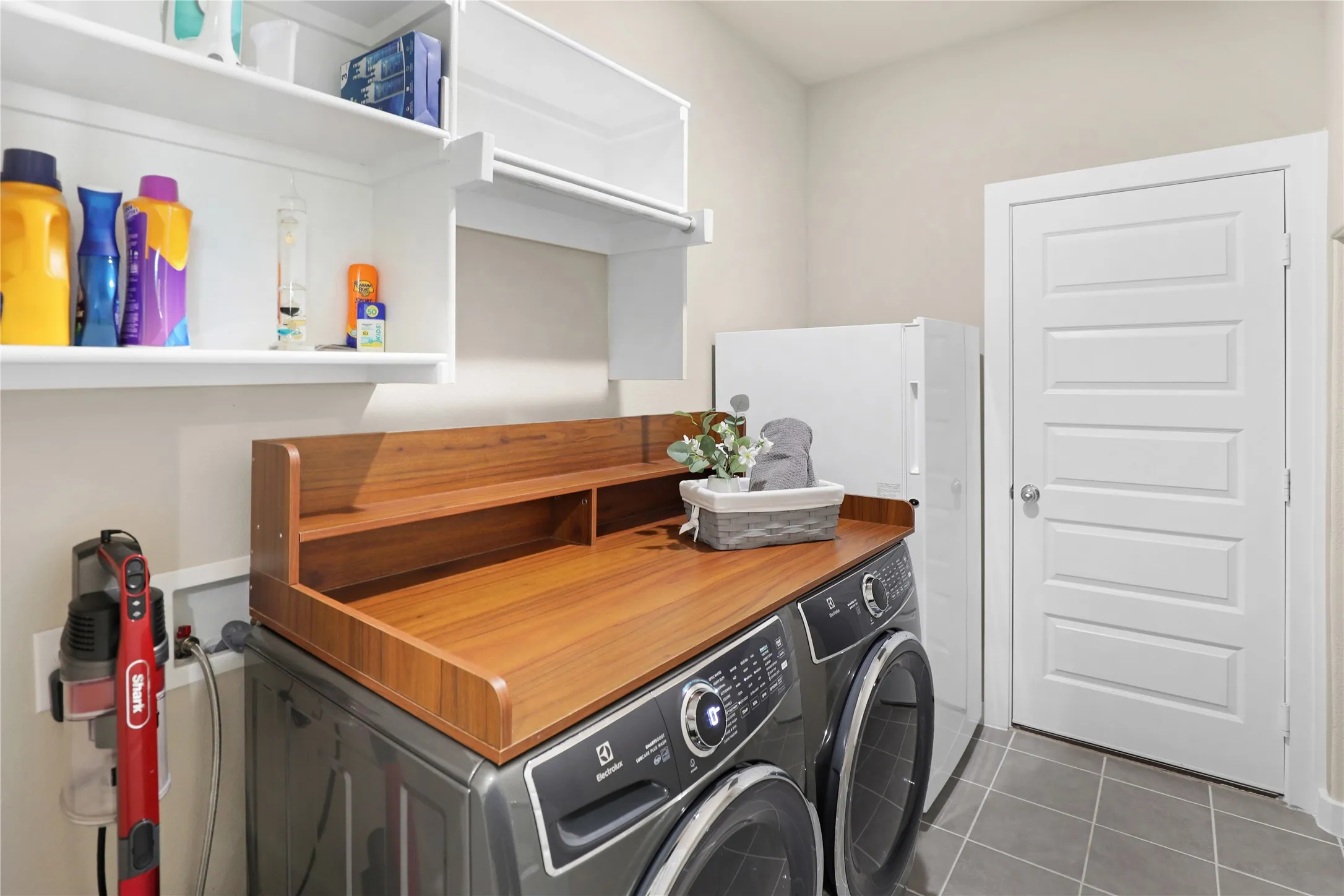Dedicated laundry area featuring a wood-finish countertop, integrated shelving, and white overhead cabinetry