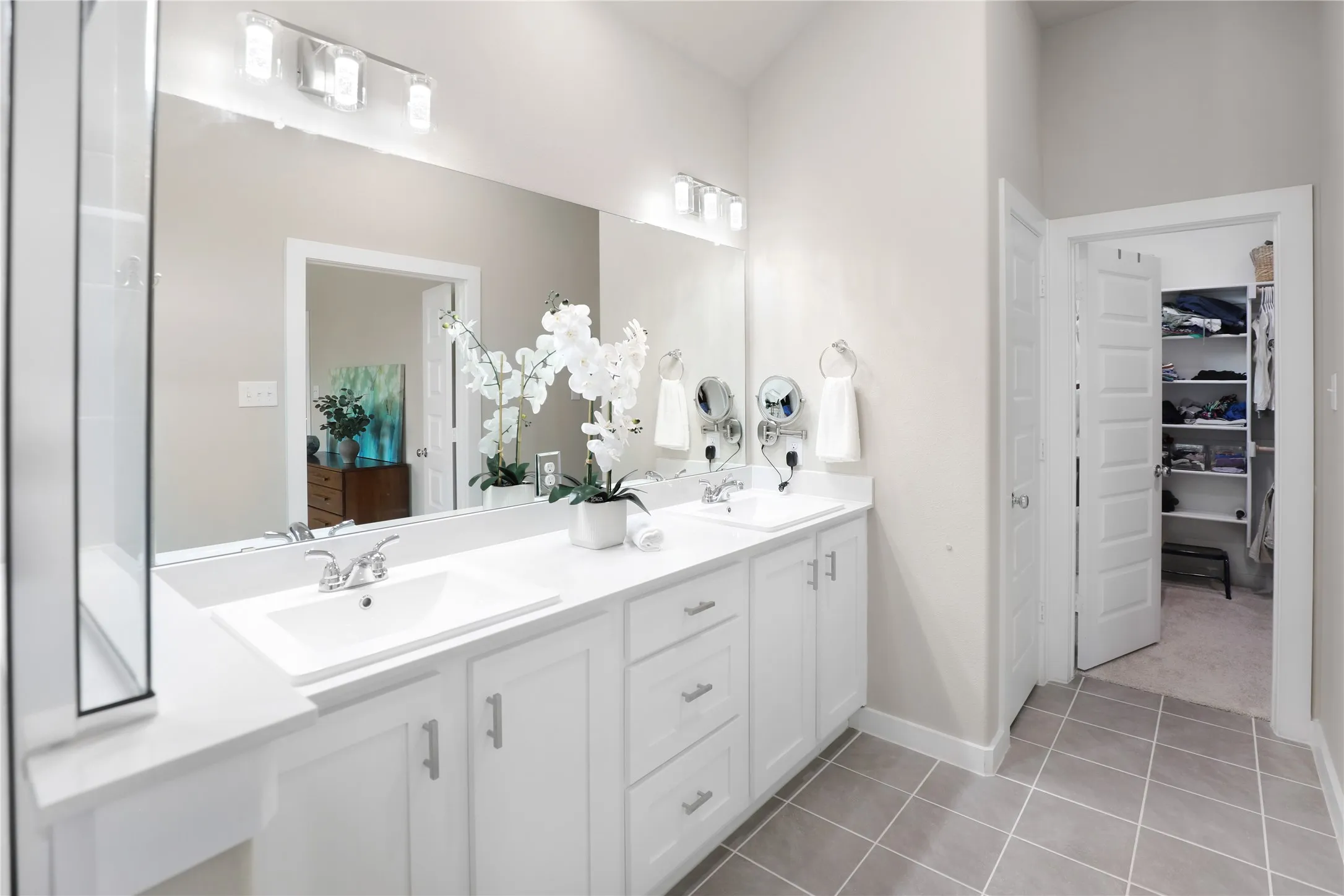 Dual vanity with white cabinetry and integrated sinks, complemented by a large mirror and overhead lighting