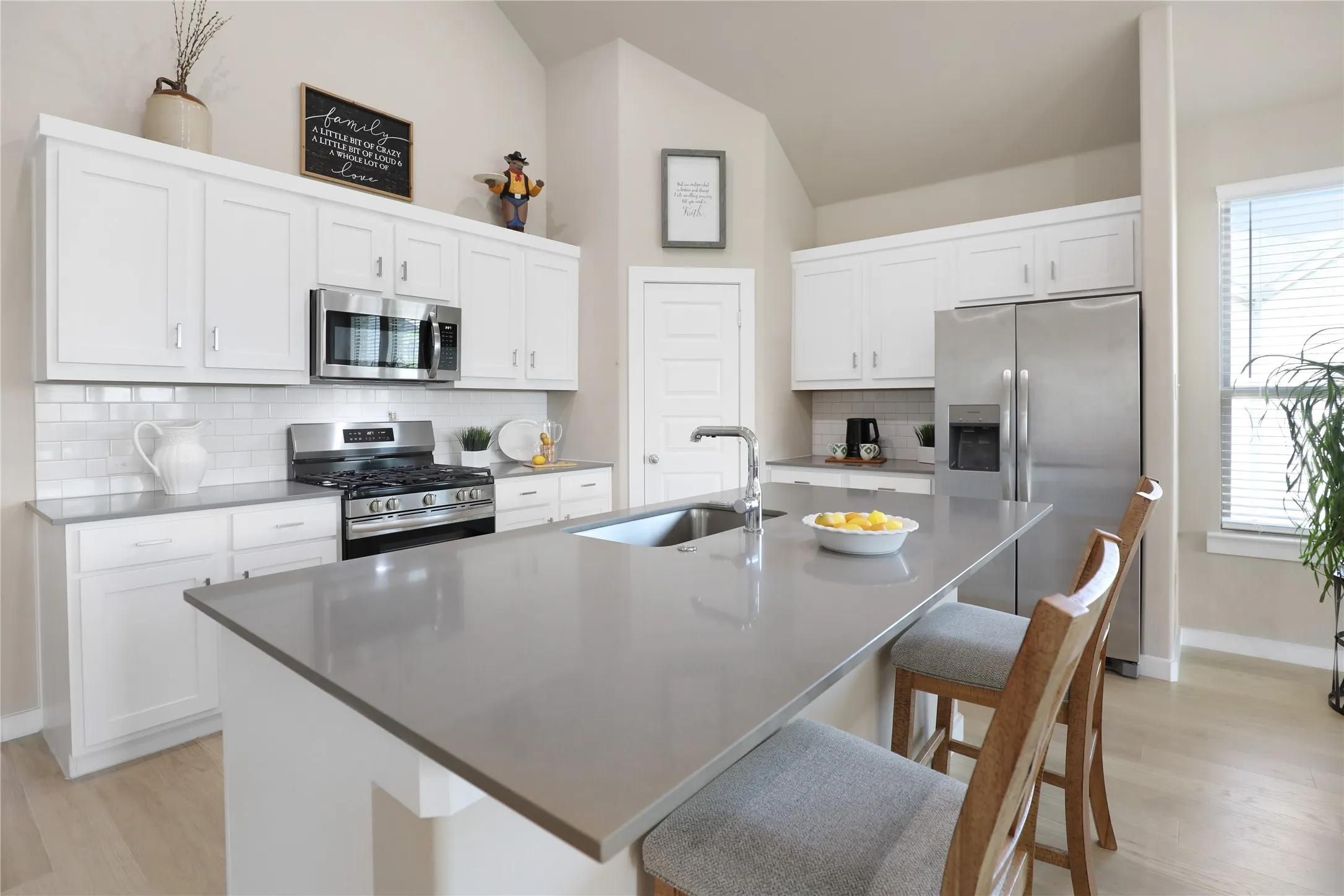 Spacious kitchen featuring white cabinetry, stainless steel appliances, a light-toned subway tile backsplash, and a large island with a double basin sink and extended countertop seating