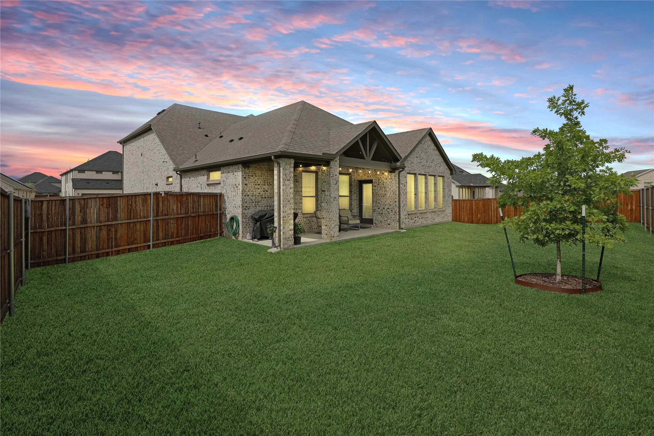 Expansive backyard featuring a manicured lawn, a young tree with a tree ring, and wood fencing