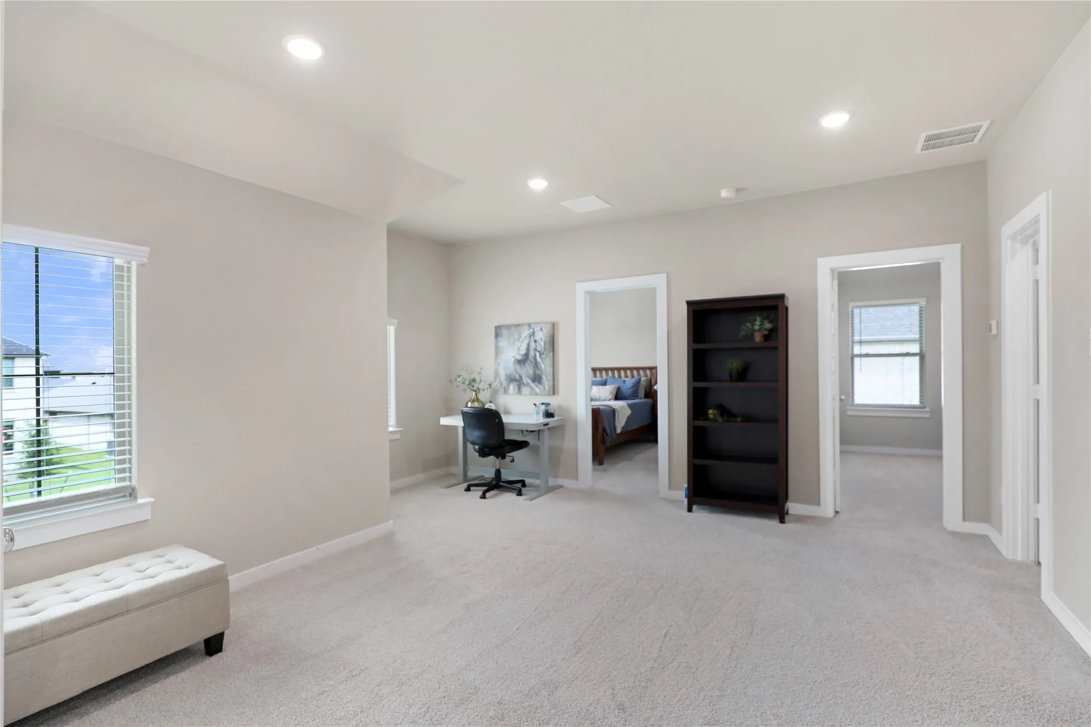 Spacious open concept room with light-colored carpeting, multiple doorways, recessed lighting, and a window with horizontal blinds