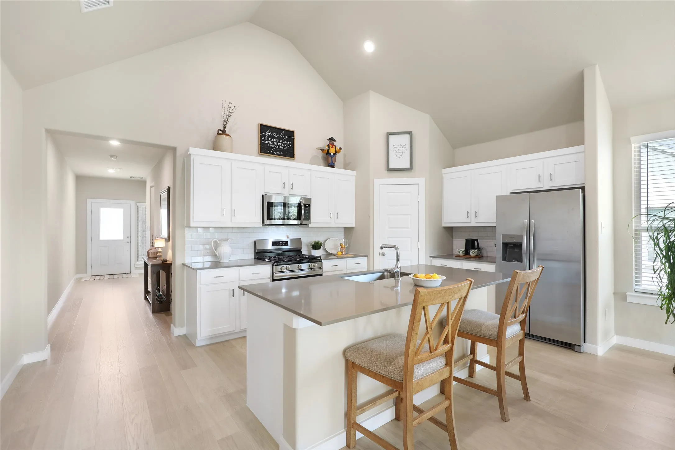 Kitchen featuring a vaulted ceiling, white shaker cabinetry, stainless steel appliances, a center island with sink, and wood-finish flooring