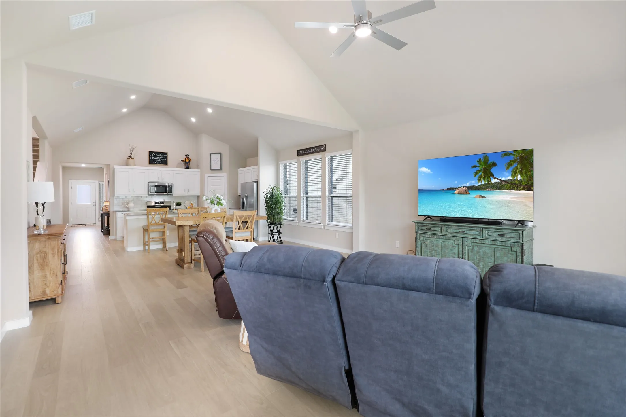 Vaulted ceiling great room featuring light wood-finish flooring, recessed lighting, a ceiling fan, and a kitchen with white cabinetry and a built-in microwave