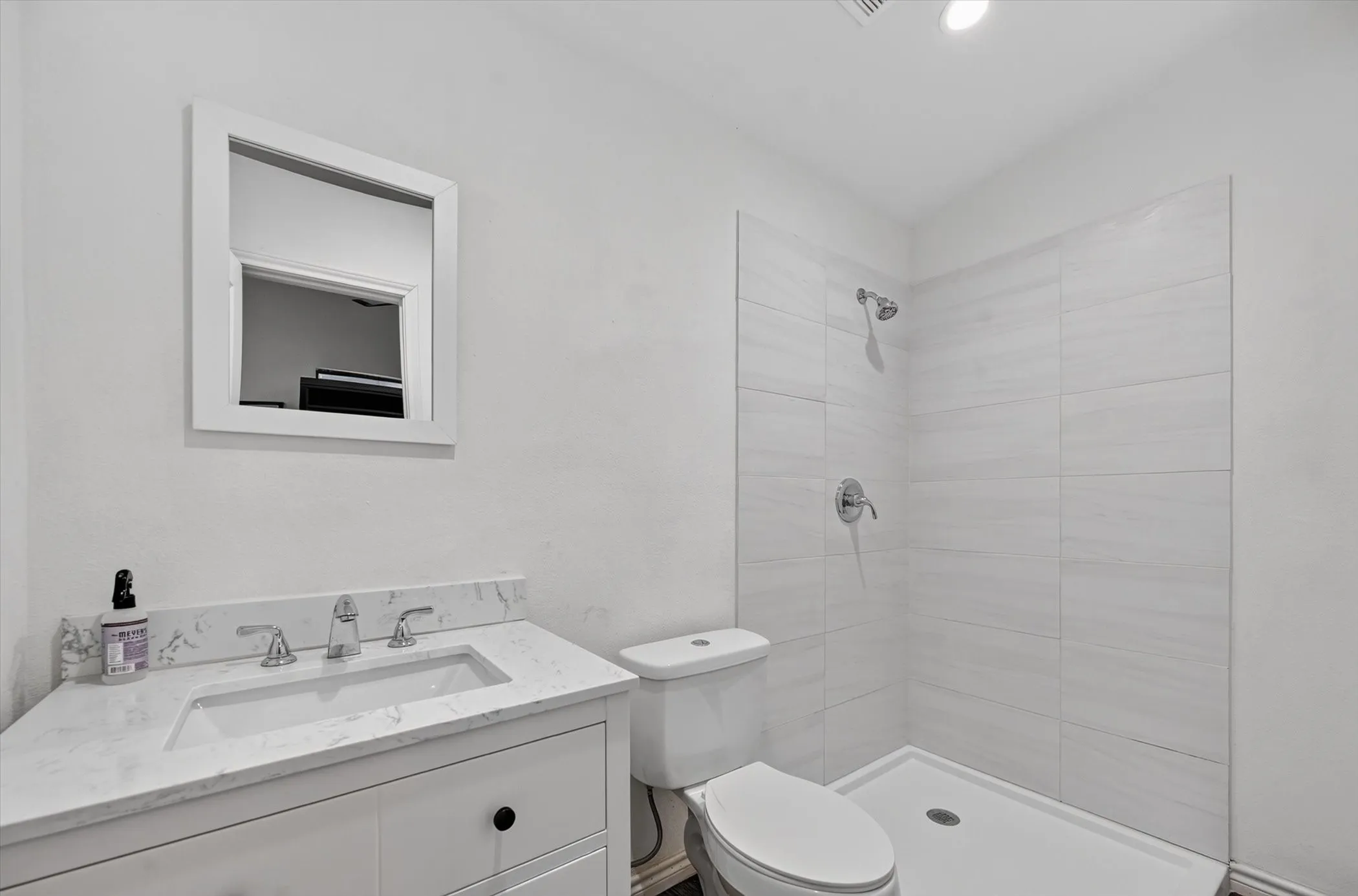 Modern bath featuring a vanity with a white countertop and integrated sink, a frameless shower with tile surround, and a toilet