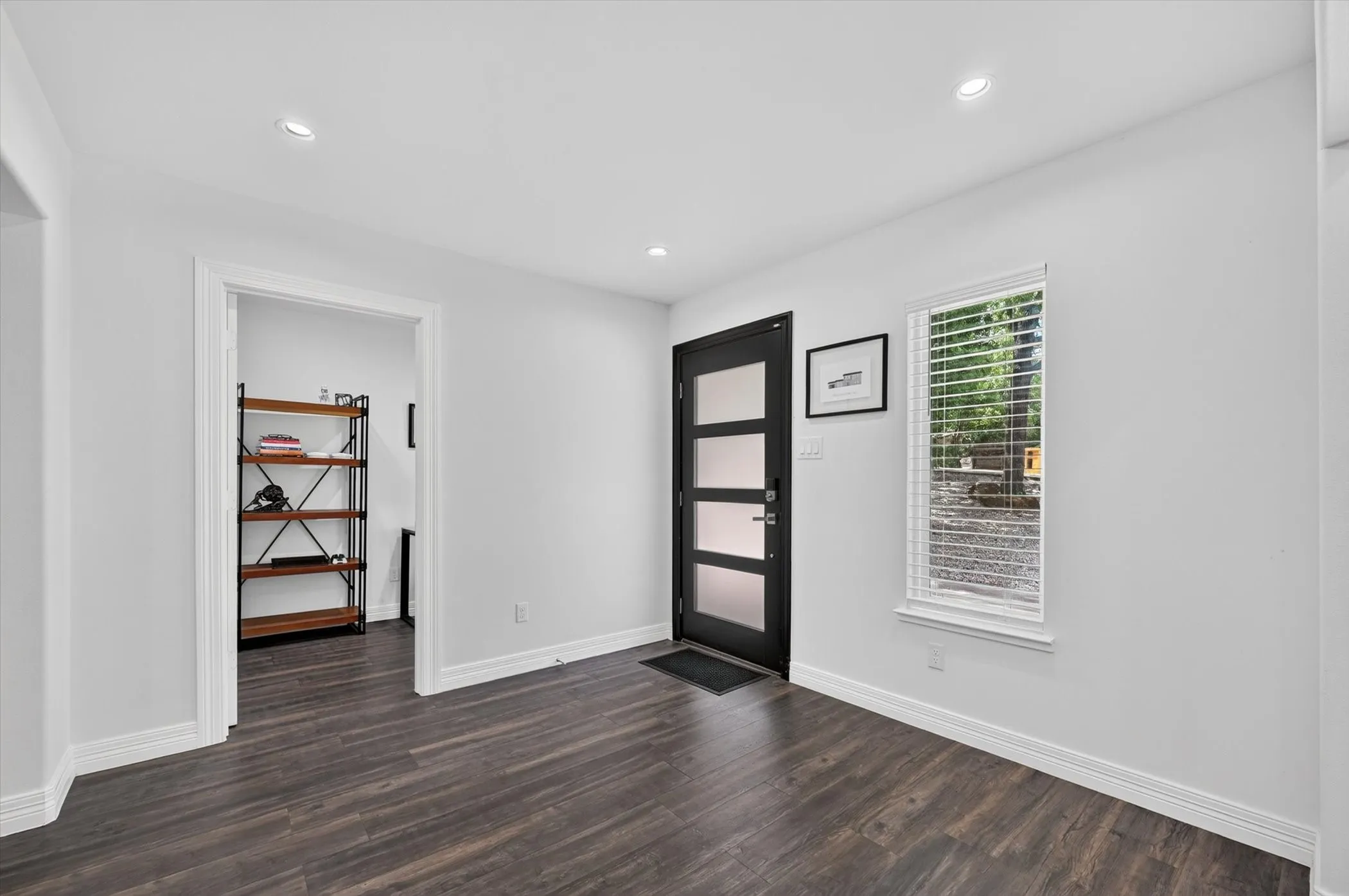 Modern entryway featuring dark wood-finish flooring, a contemporary door with frosted glass panels, and a vertical window with blinds