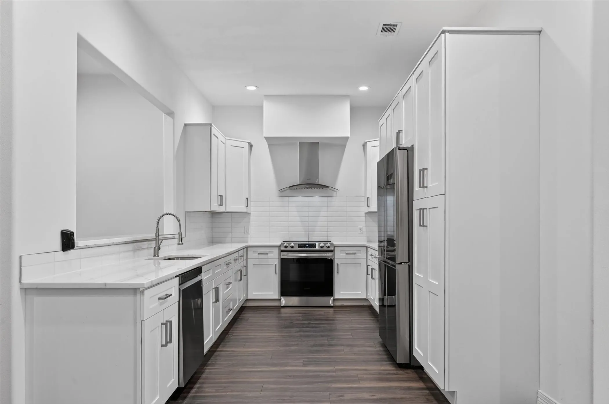 Contemporary kitchen featuring white shaker cabinetry, stainless steel appliances, a subway tile backsplash, light stone countertops, and dark wood-finish flooring