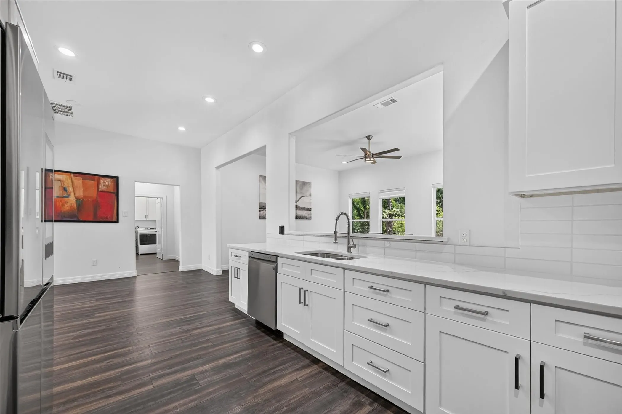 Bright kitchen featuring white shaker cabinetry, stainless steel dishwasher, and a gooseneck faucet