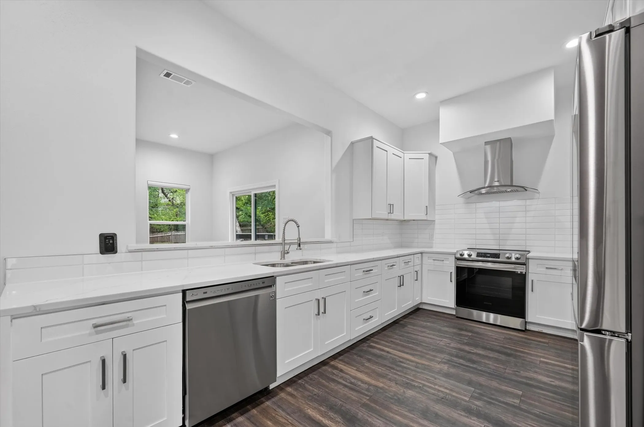 Contemporary kitchen featuring white shaker cabinetry, stainless steel appliances, quartz countertops, a subway tile backsplash, and dark wood-finish flooring