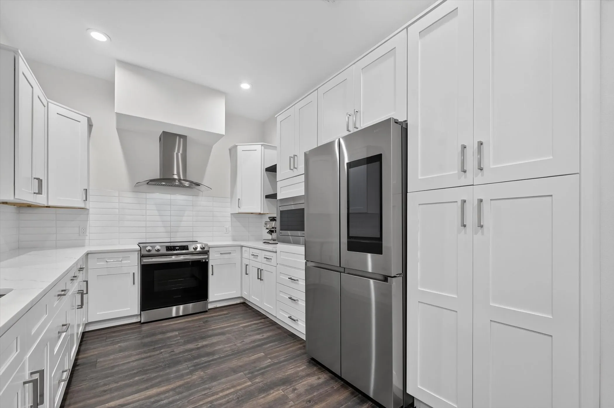 Modern kitchen featuring white shaker cabinetry, stainless steel appliances, a stainless steel range hood, white subway tile backsplash, and wood-finish flooring