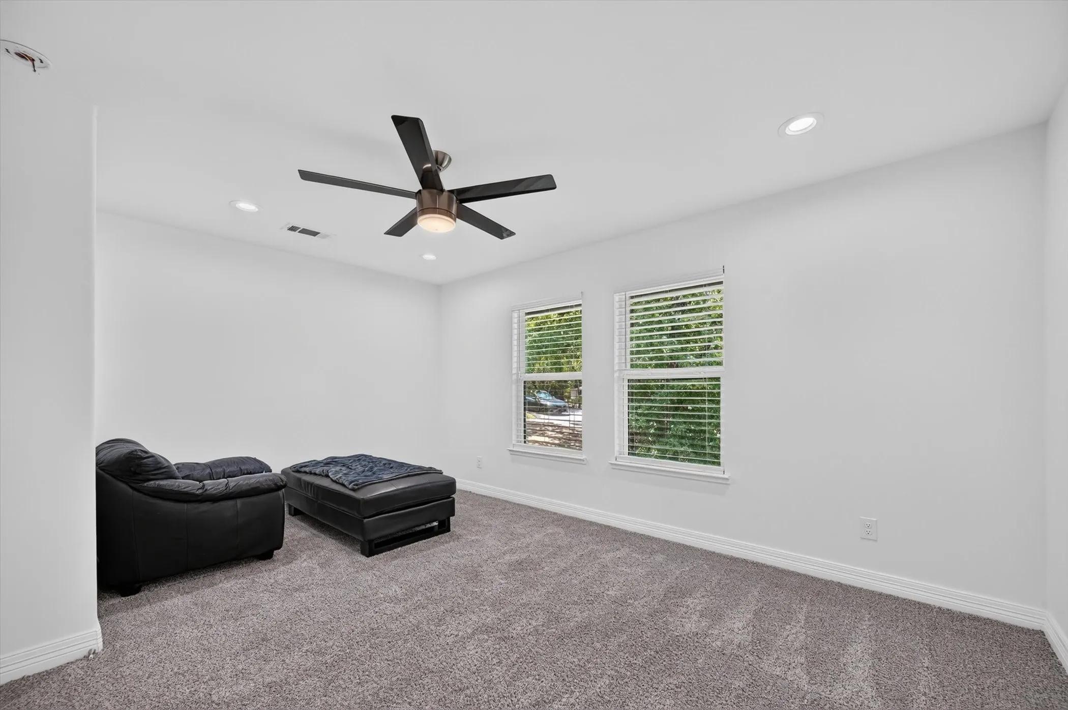 Spacious room featuring neutral carpeting, two windows with blinds, a ceiling fan with integrated lighting, and recessed lighting