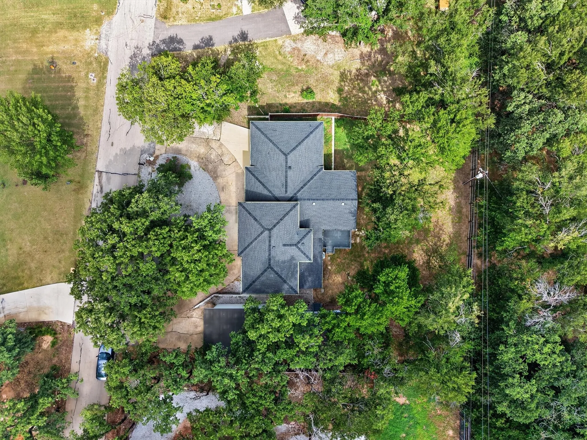 Property situated on a treed lot with a dark shingle roof and a concrete driveway