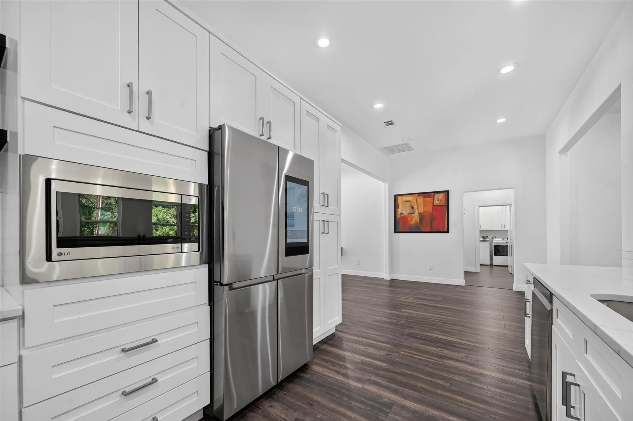 Contemporary kitchen featuring white cabinetry, stainless steel appliances, dark wood-finish flooring, recessed lighting, and light-toned countertops