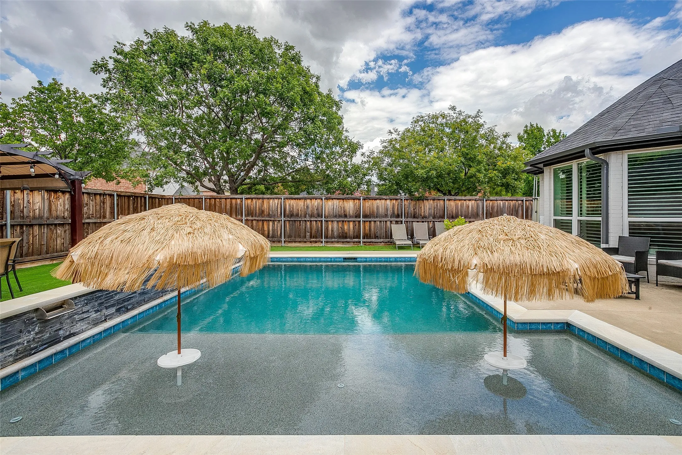 Resort style pool featuring a built-in tanning ledge topped with tiki-style straw umbrellas.