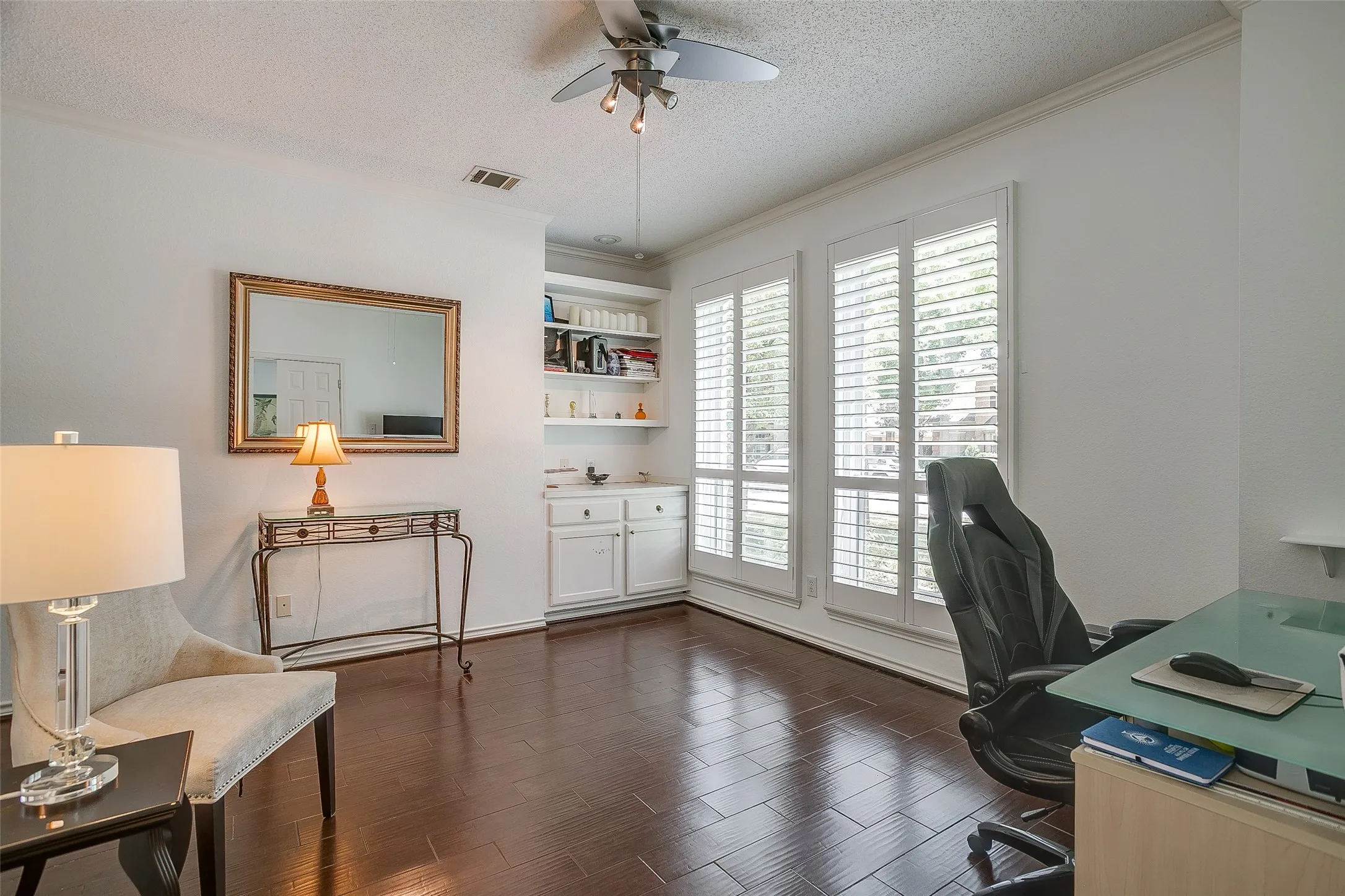 Office with built in cabinets and shelving, plantation shutters and a ceiling fan.