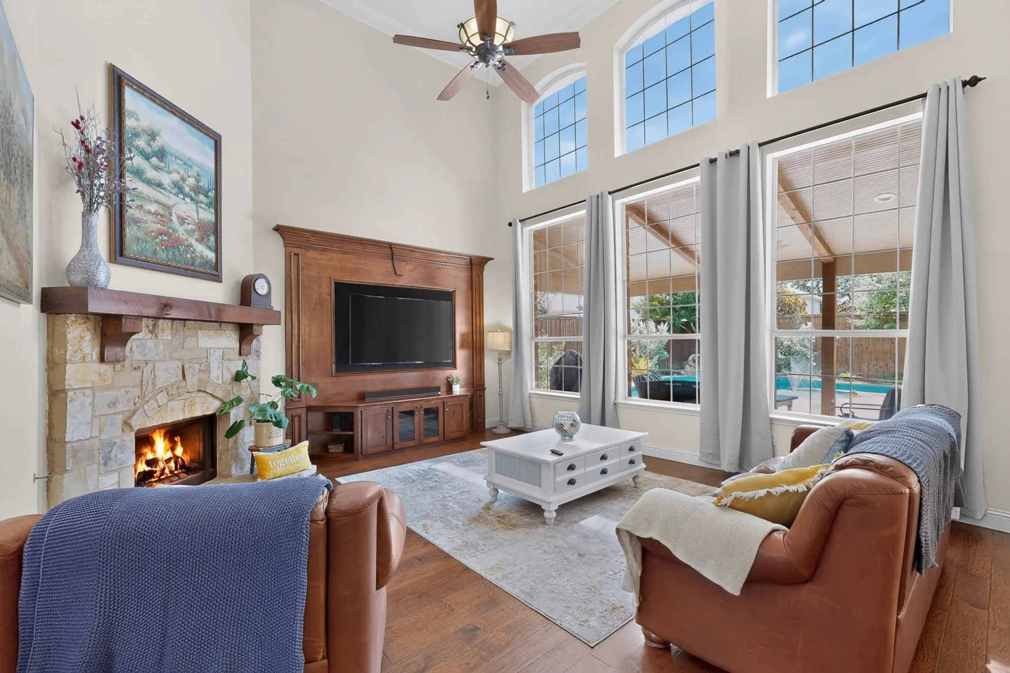TWO STORY LIVING ROOM WITH BUILT IN ENTERTAINMENT CENTER, CUSTOM STONE FRONT FIREPLACE, AND TALL WINDOWS FOR PLENTY OF NATURAL LIGHT