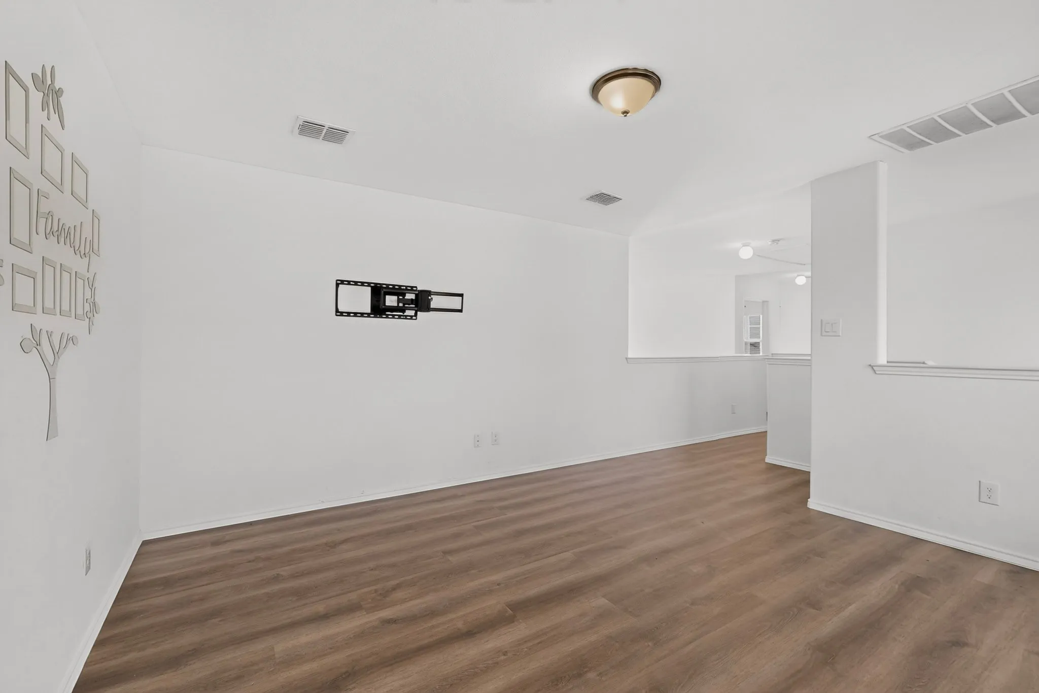 Spacious interior room featuring wood-finish flooring, white walls, and a recessed wall for a television mount